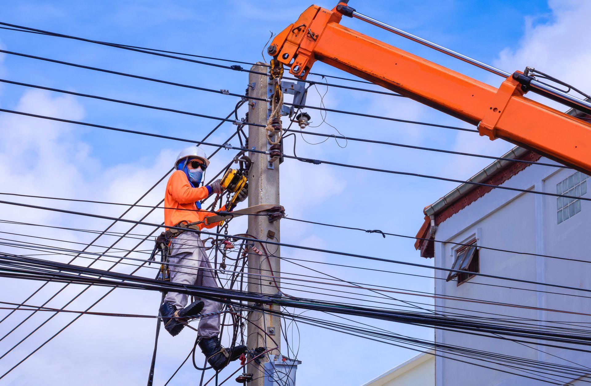 Lineman in orange suit working on power lines from a crane.