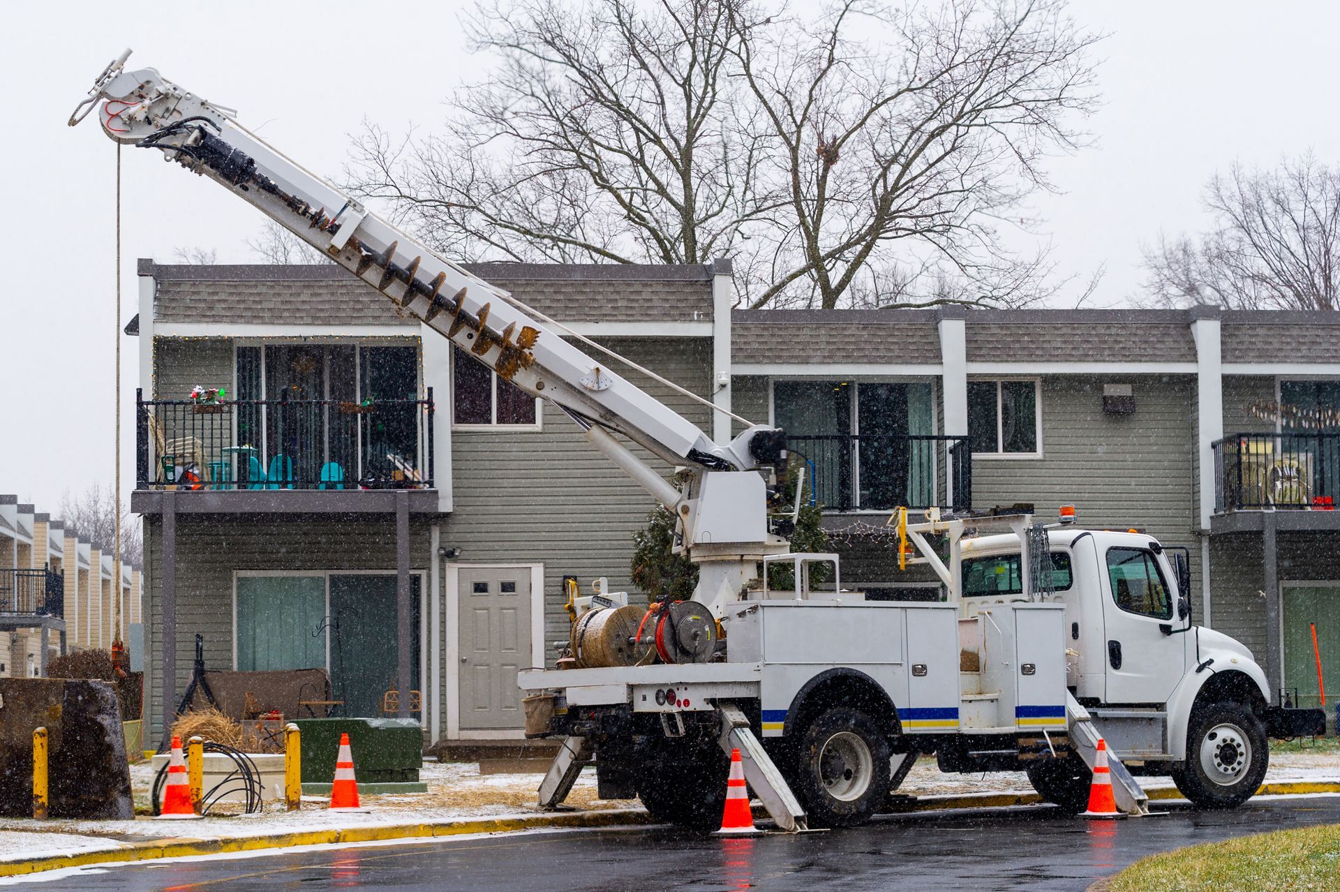 Utility truck with an extended arm, working near an apartment building in snowy conditions.