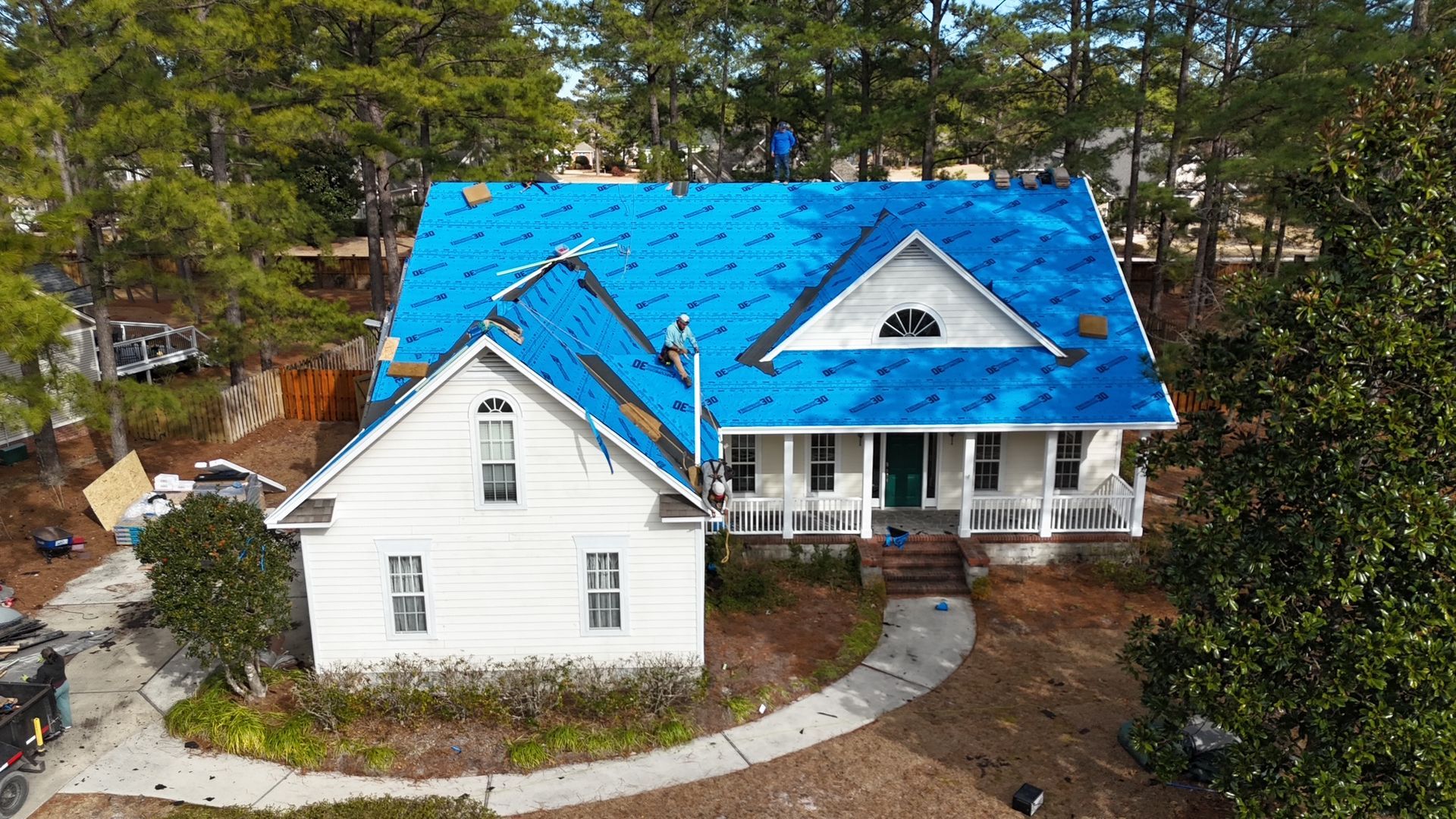 An aerial view of a white house with a blue covering on the roof.