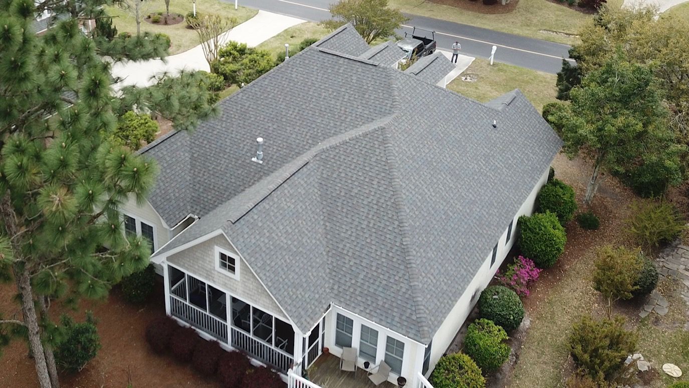 An aerial view of a white house with a gray roof surrounded by trees and bushes.
