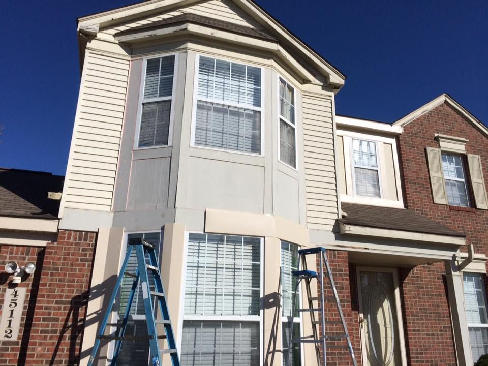 House exterior under construction, with ladders, brick, siding, and painted trim.