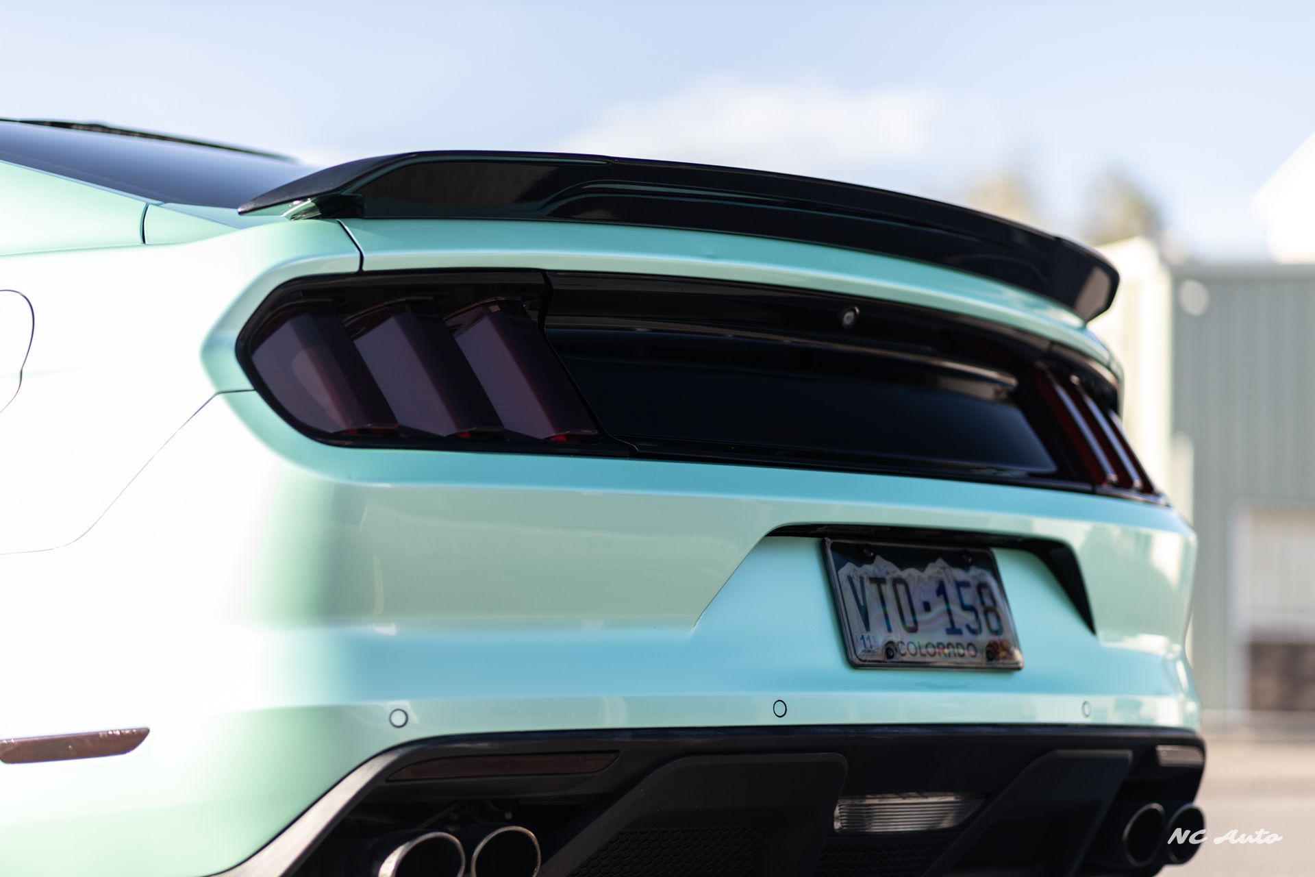 Mint green Ford Mustang rear end with black spoiler and taillights.