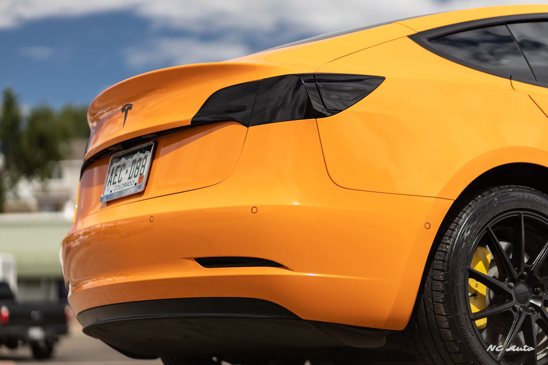 Yellow Tesla car rear, black tinted lights, black wheels with yellow calipers, outdoors.