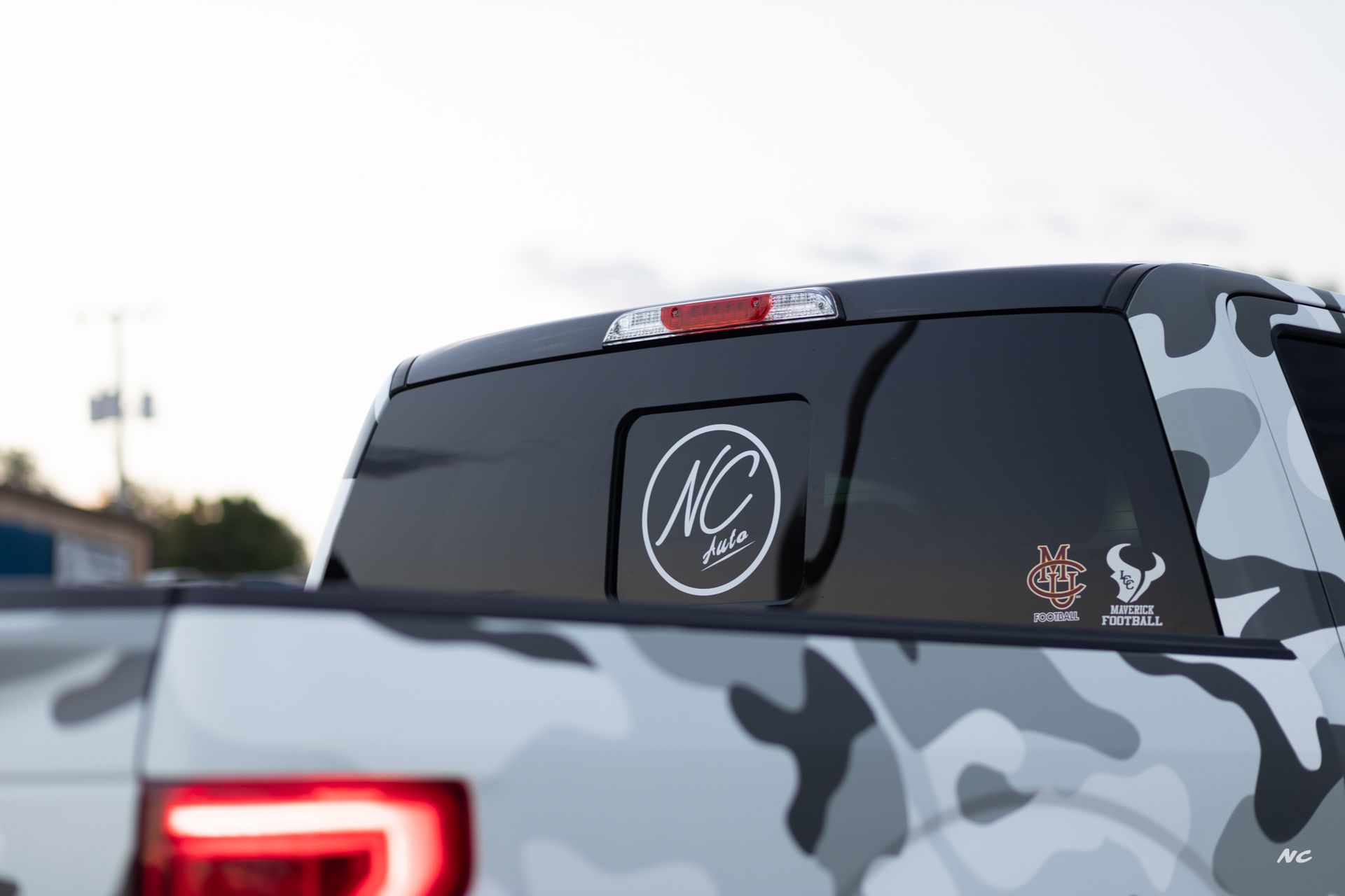 Truck rear window with stickers; white and gray camouflage wrap.