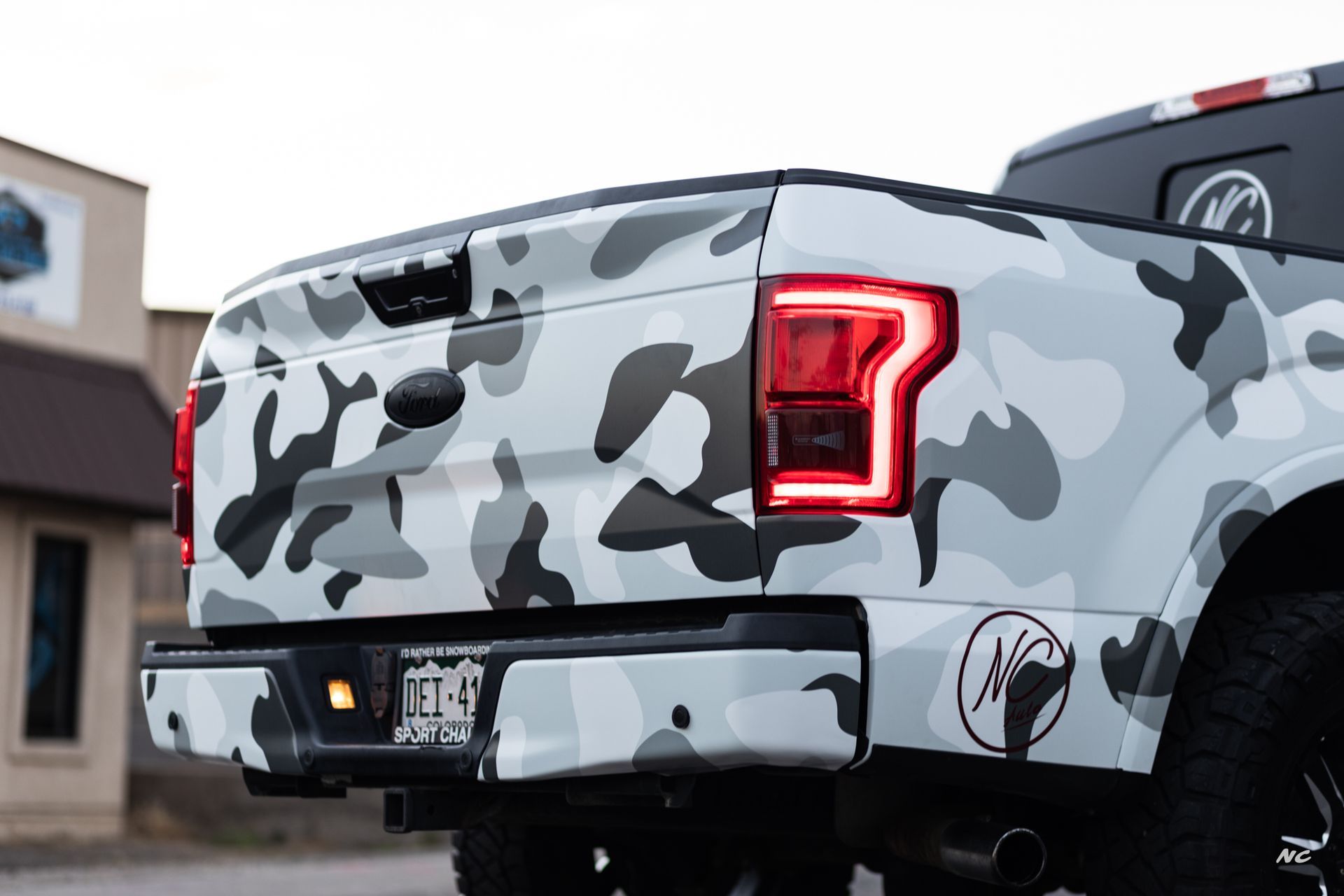 White and gray camouflage-wrapped Ford F-150 truck with black accents, rear view, Colorado license plate.