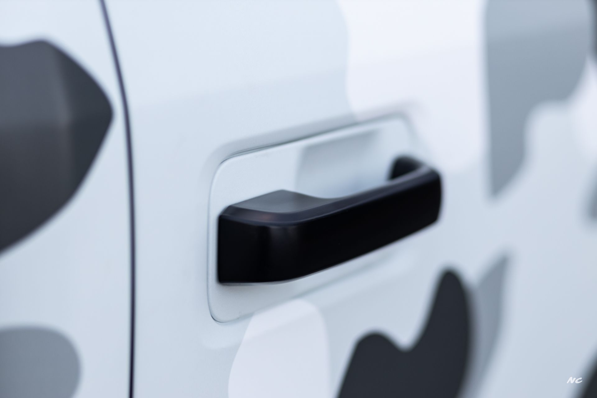 Black car door handle on a white vehicle with gray camouflage pattern.
