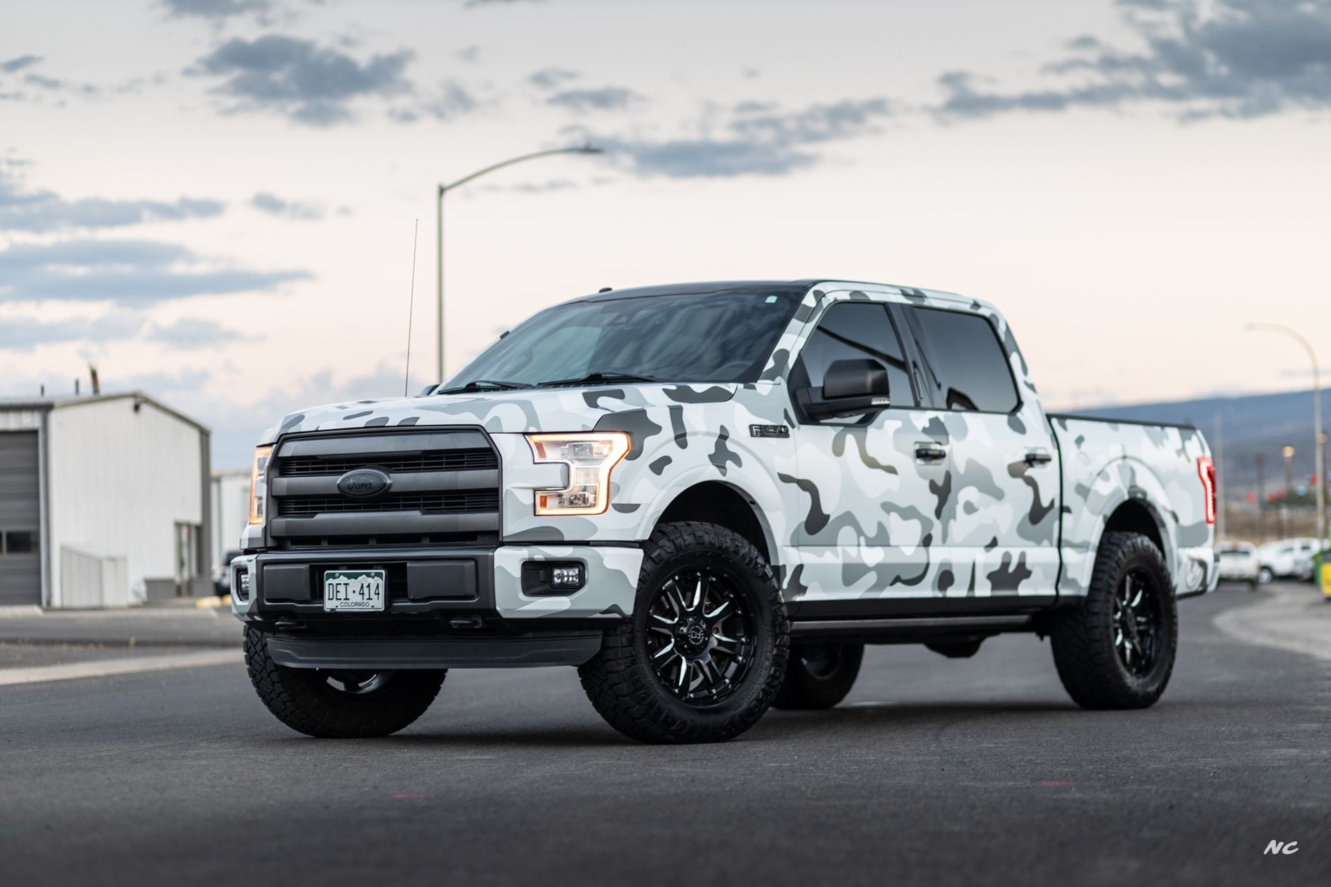 White camouflage Ford F-150 pickup truck with black wheels, parked on asphalt.