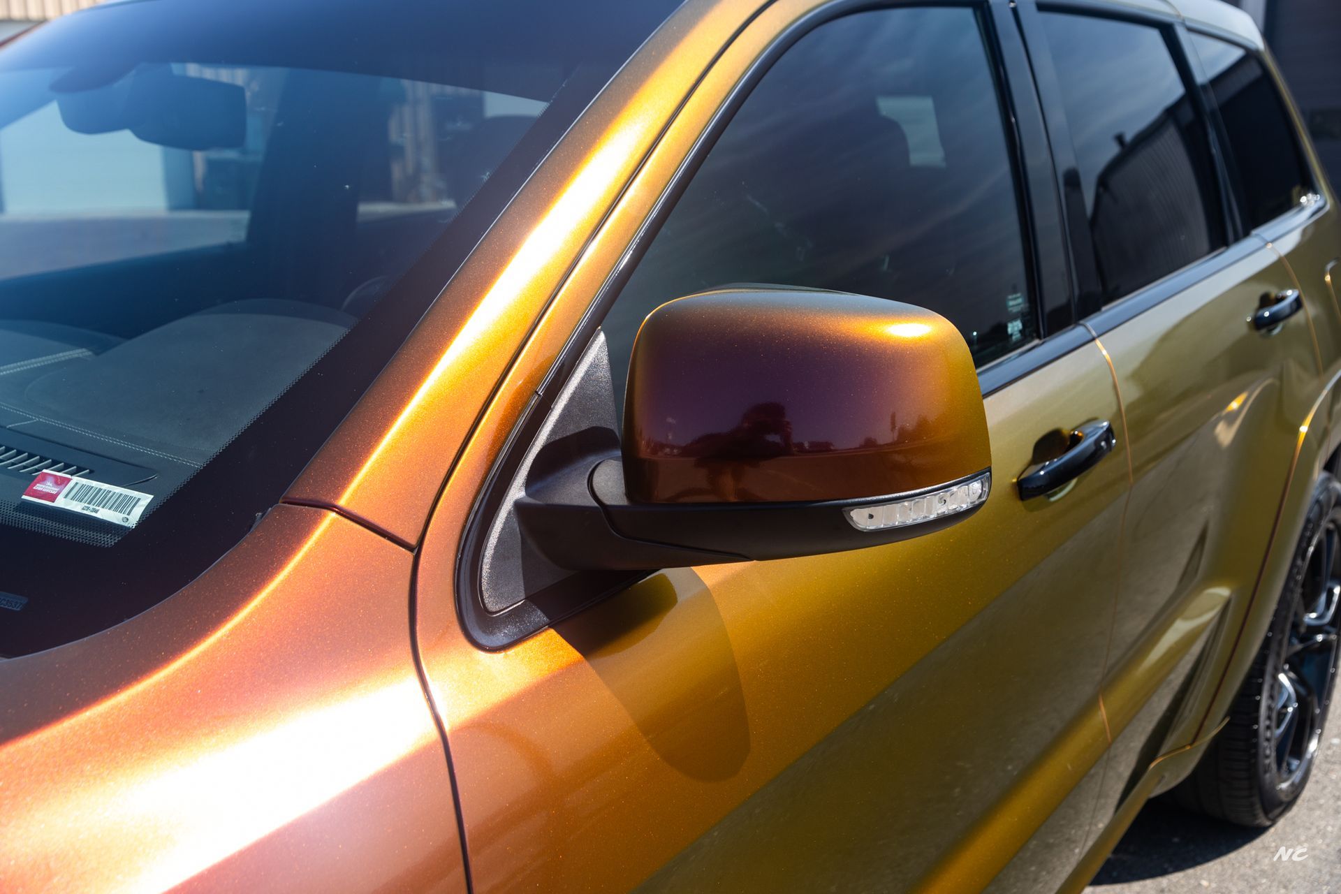 A gold and purple color-shifting SUV's side mirror, with the windshield and a partial view of the black window.