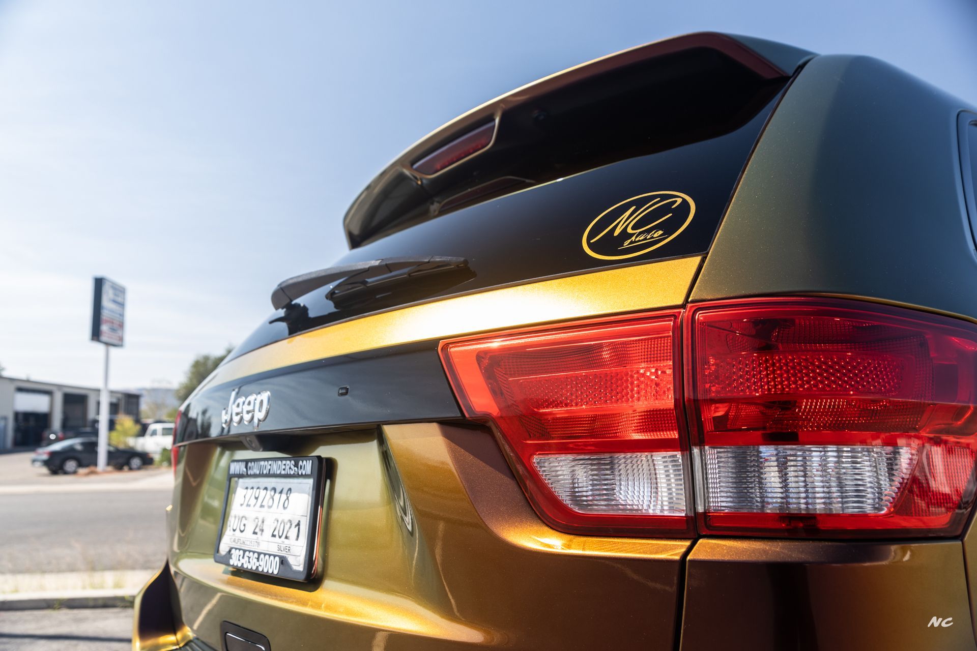 Rear of a gold and black Jeep SUV with a license plate and a logo on the rear window.