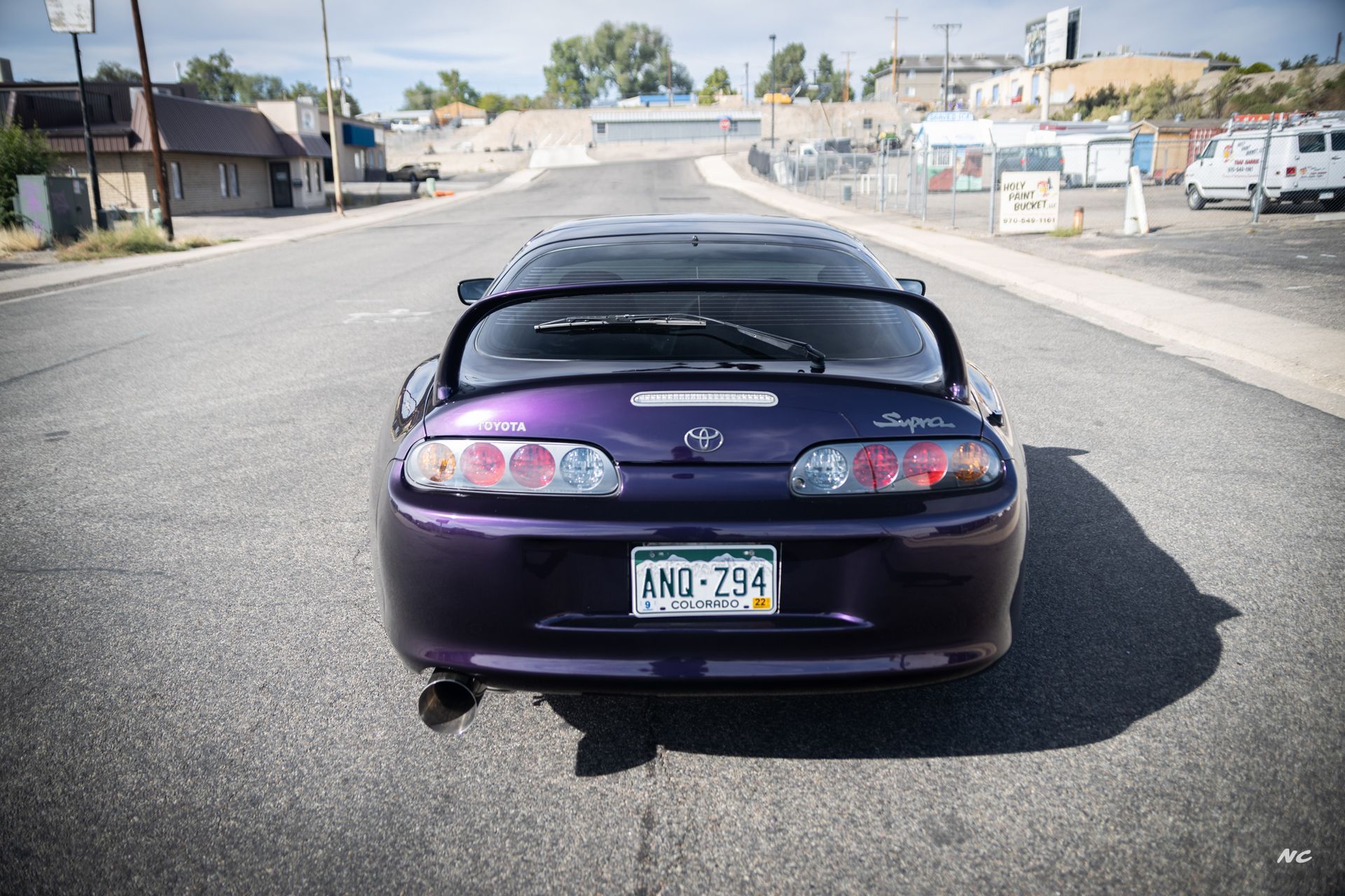 Rear view of a purple Toyota Supra with a spoiler, parked on a road. Colorado license plate.