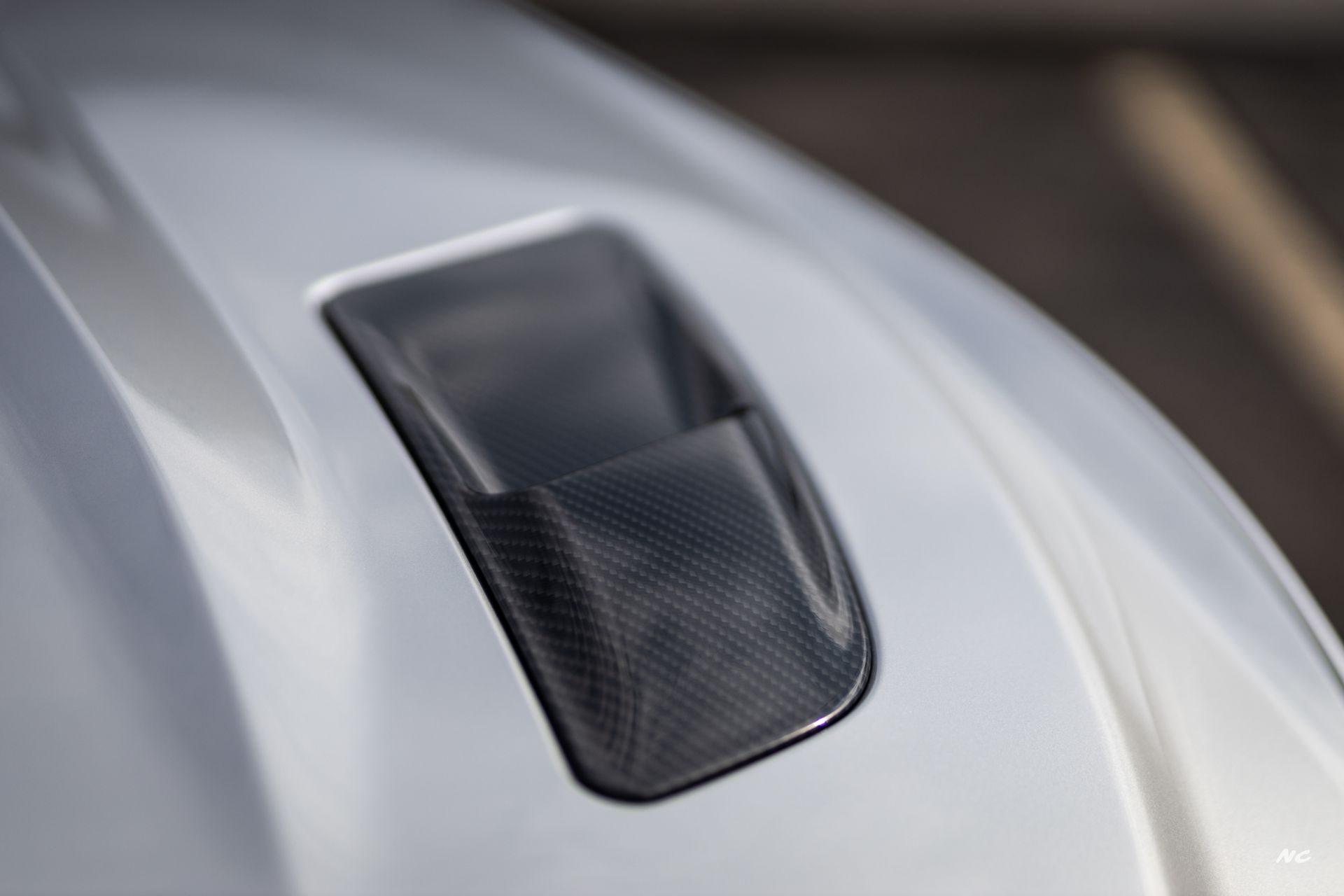 Close-up of a silver car hood with a black carbon fiber air vent.