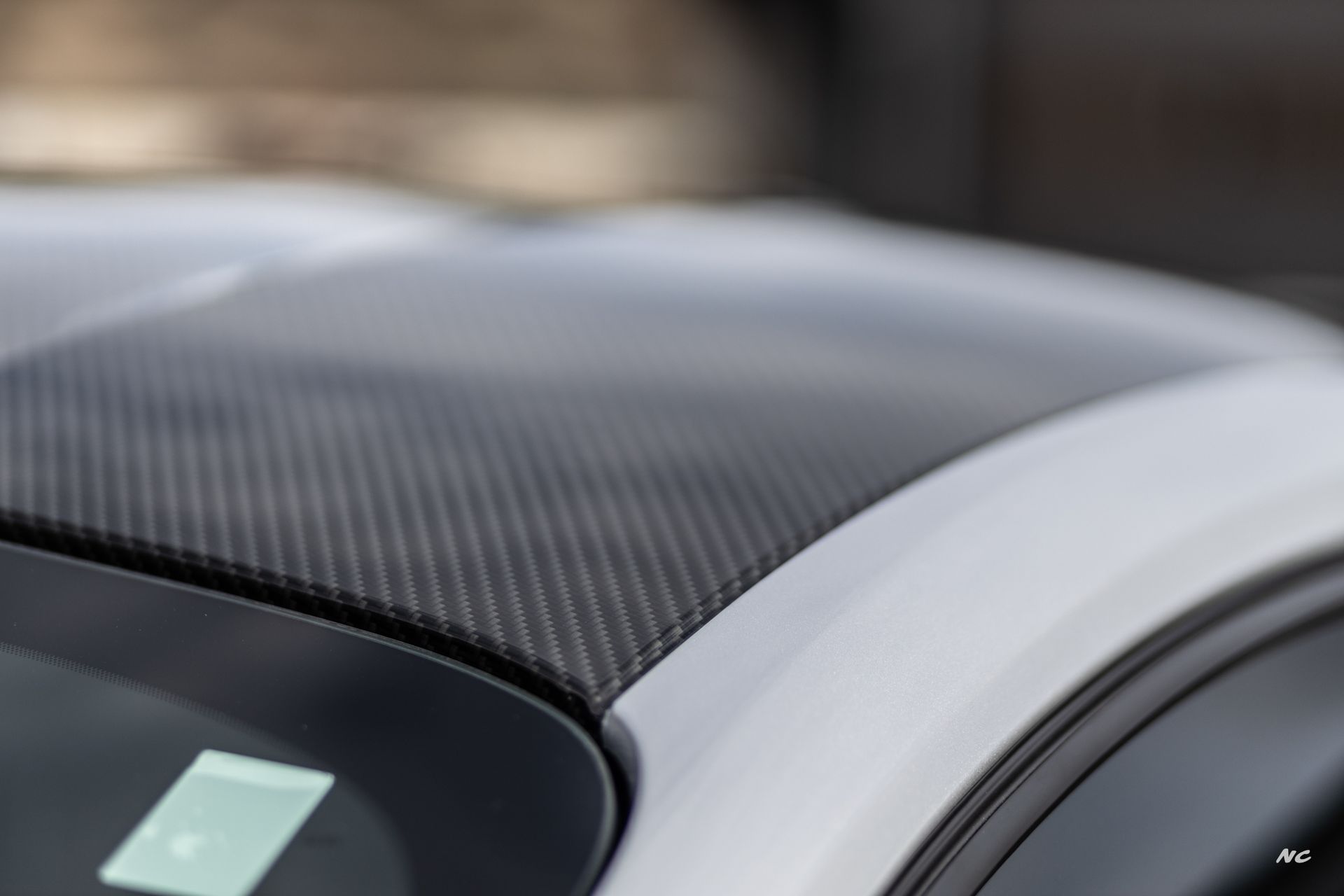 Close-up of a white car roof with a carbon fiber section. The roof is slightly curved and in focus.