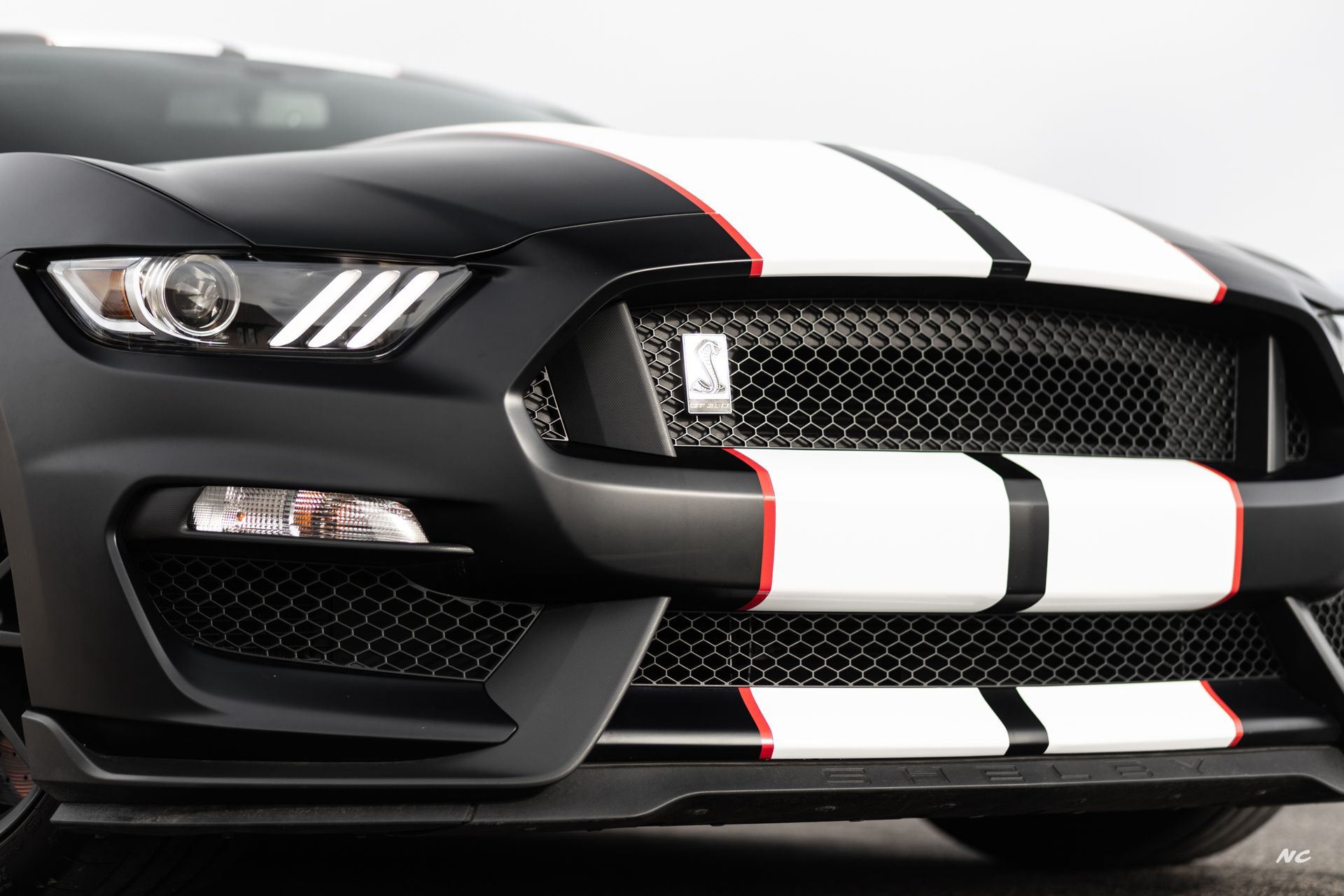 Black Shelby GT350 Mustang with white racing stripes, red accents, and black grille.