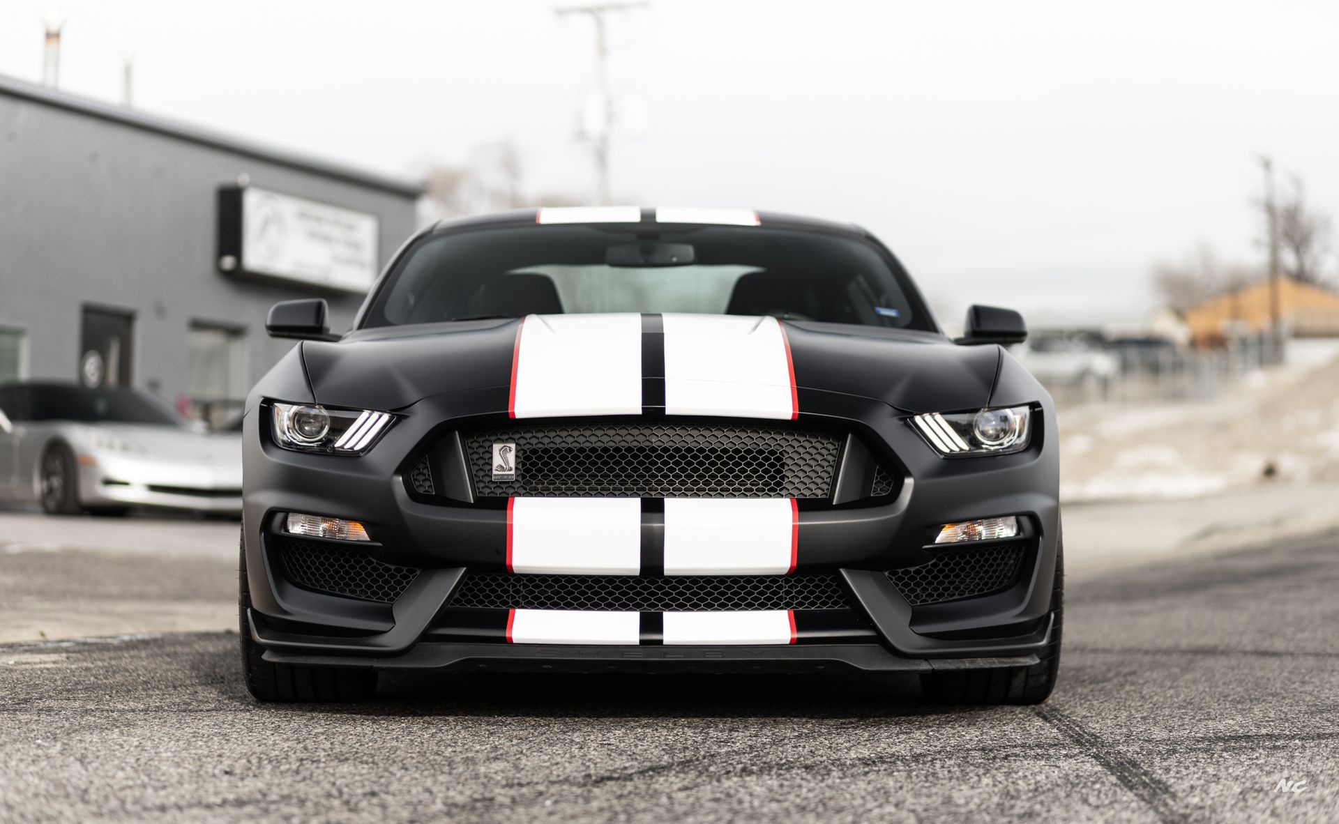 Black Ford Mustang with white racing stripes, parked in front of a building.