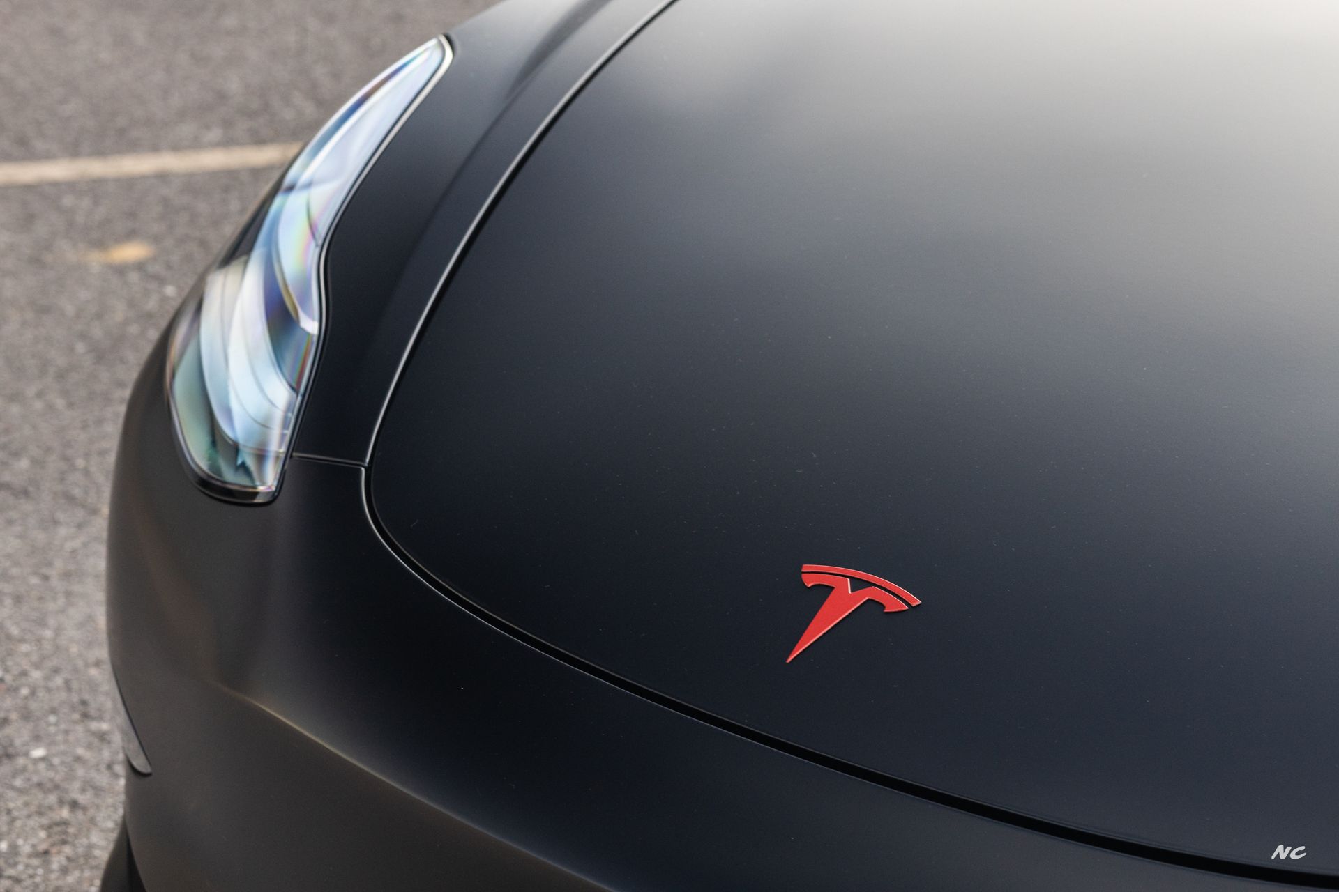 Matte black Tesla car hood with red logo and headlight.