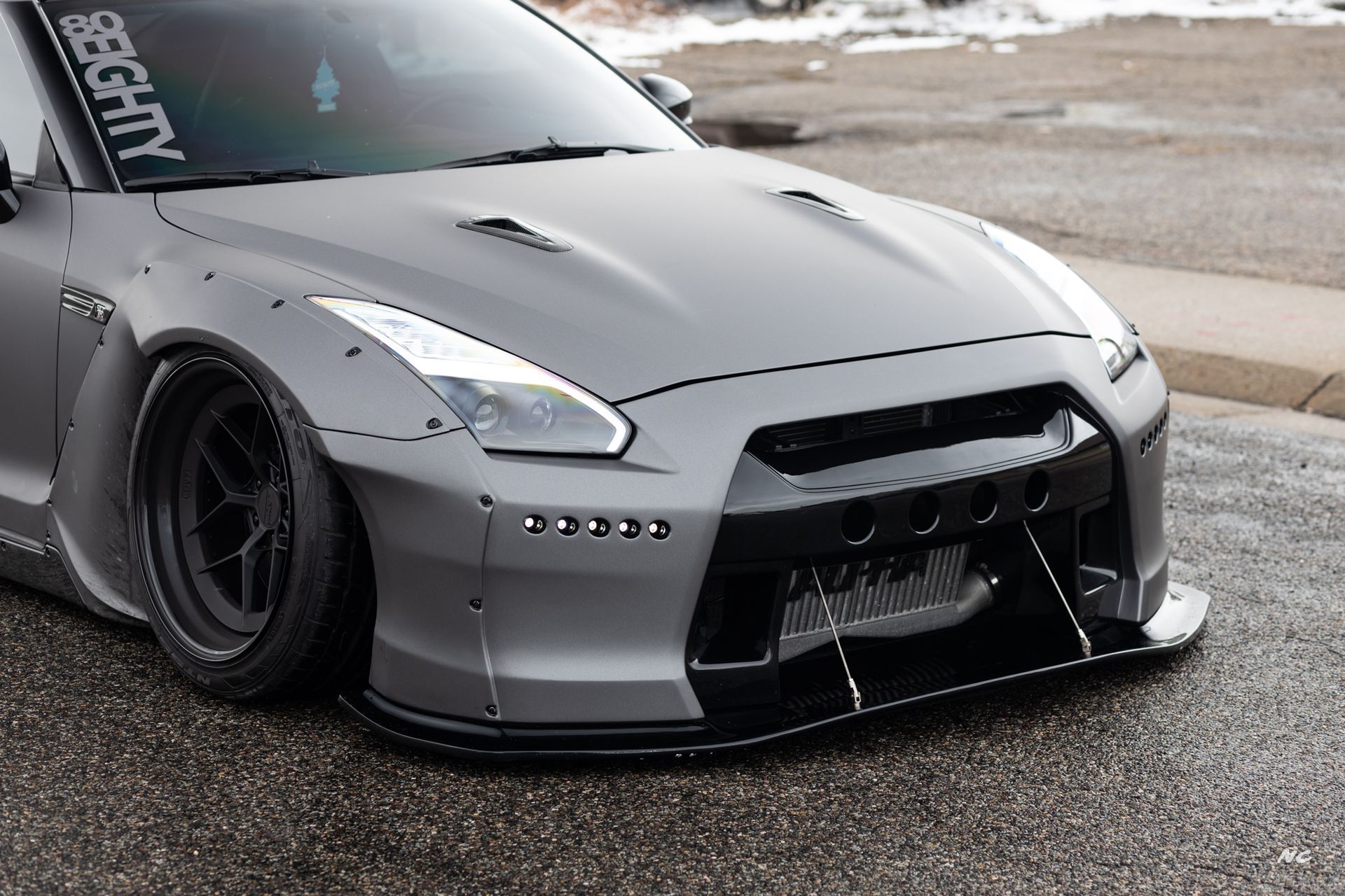 Gray Nissan GT-R sports car with modified body kit and lowered suspension, parked on pavement.