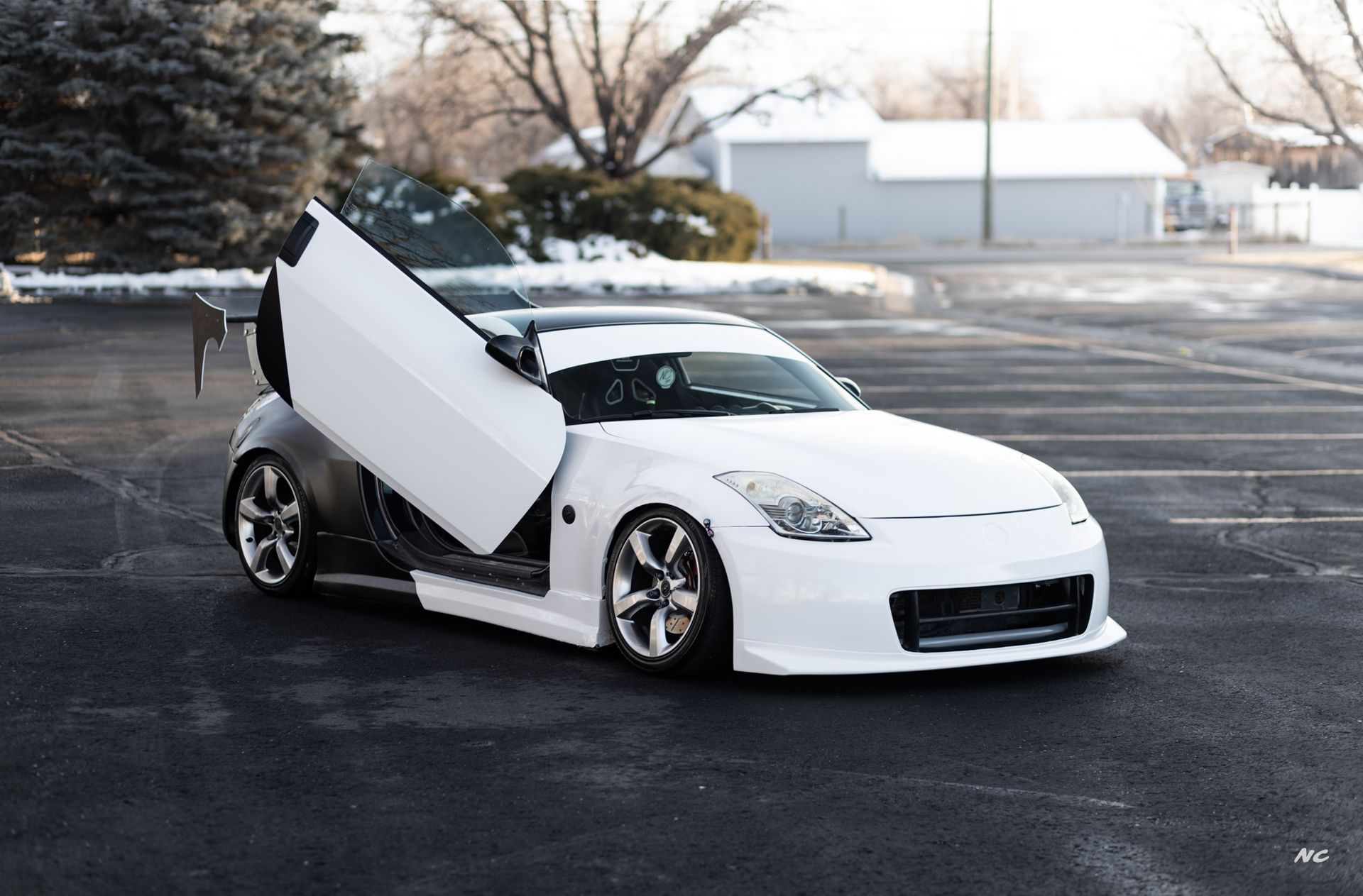 White Nissan 350Z with gullwing doors open, parked outdoors in a snowy setting.