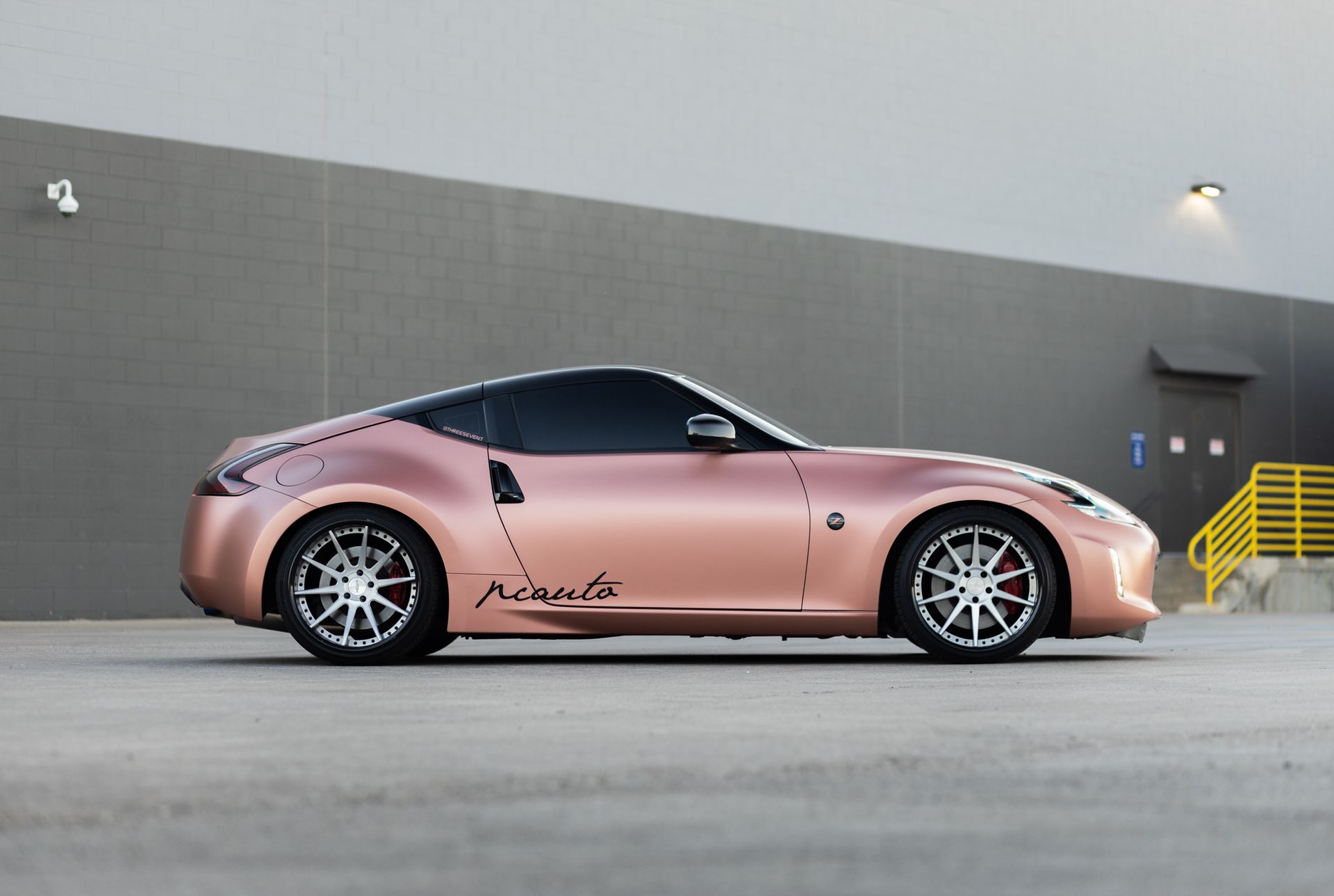 Rose gold Nissan 370Z sports car parked in front of a gray building.