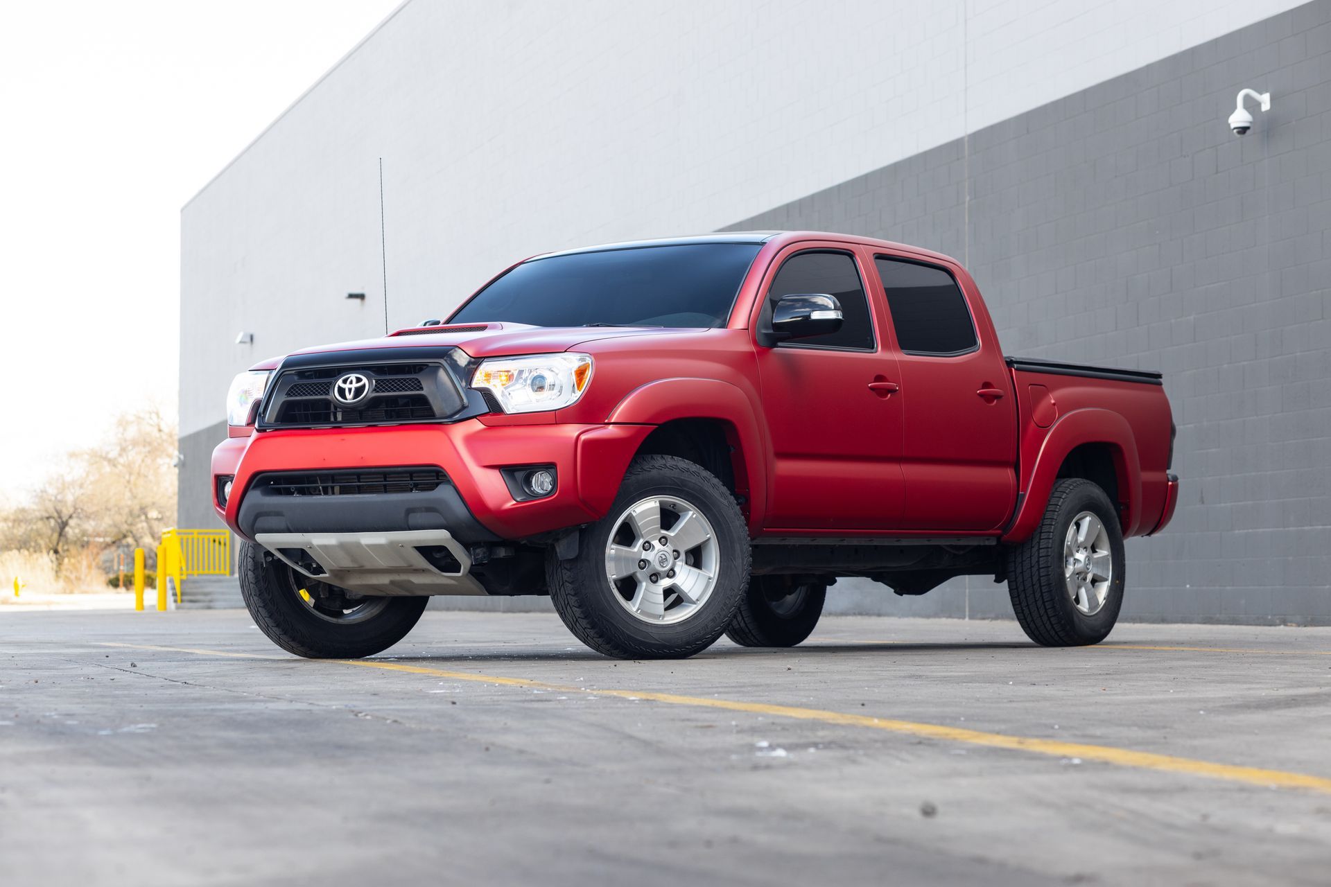 Red Toyota Tacoma truck parked on pavement near a building.