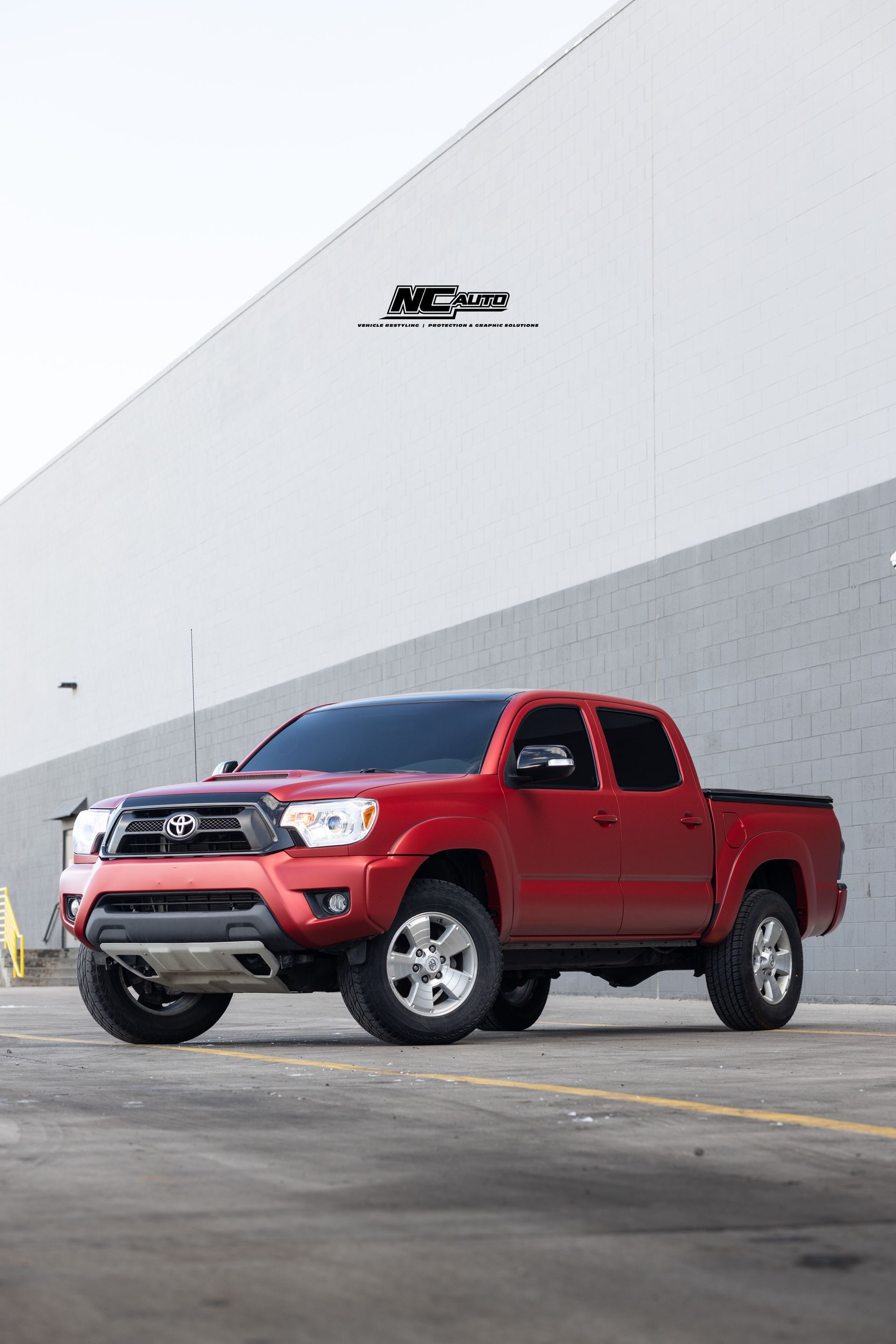 Red Toyota Tacoma truck parked in front of a white and gray building.