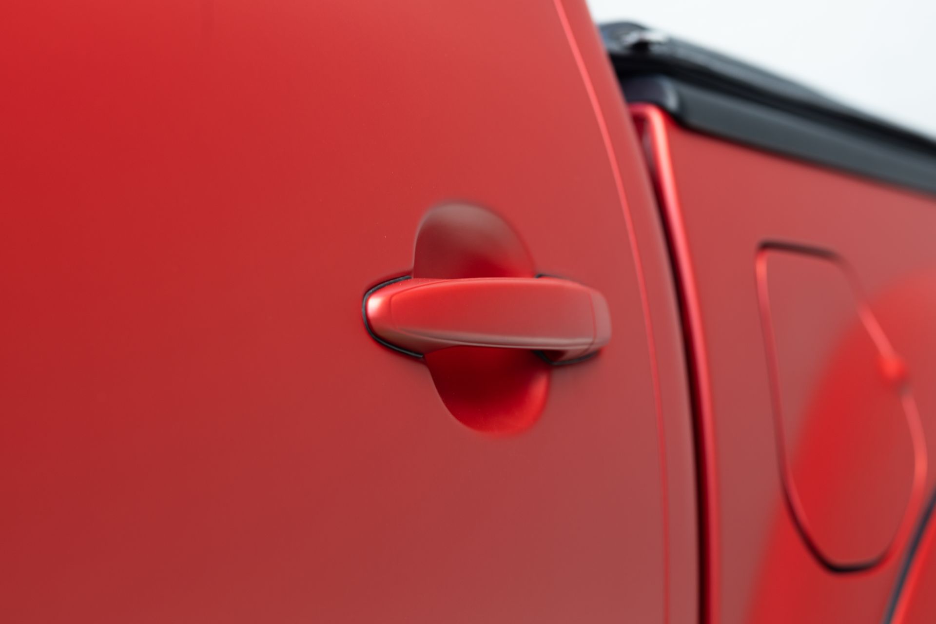 Red car door with matching handle and a portion of a black bed cover.