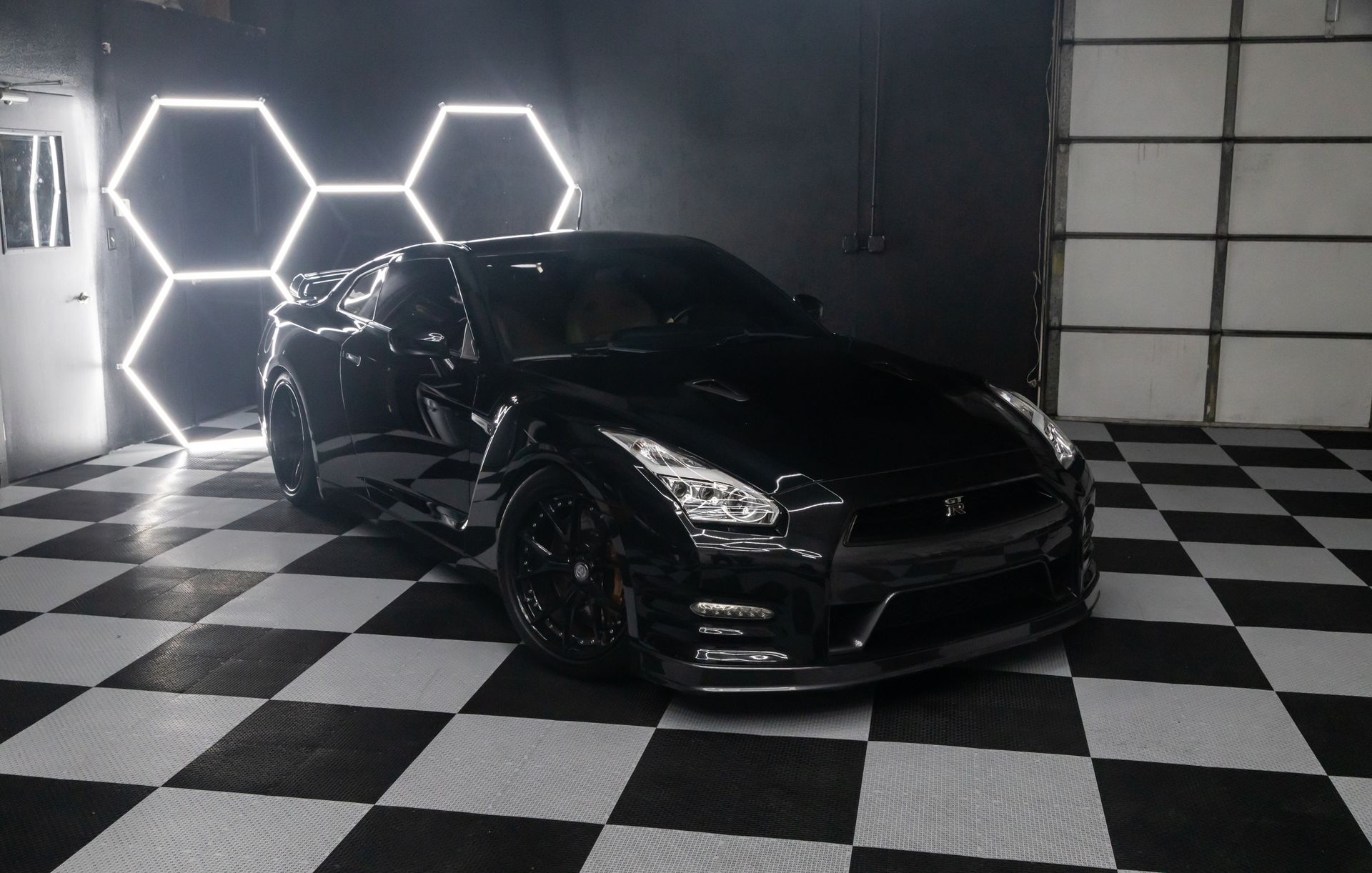 Black sports car parked on checkered floor, illuminated by hexagon lights.