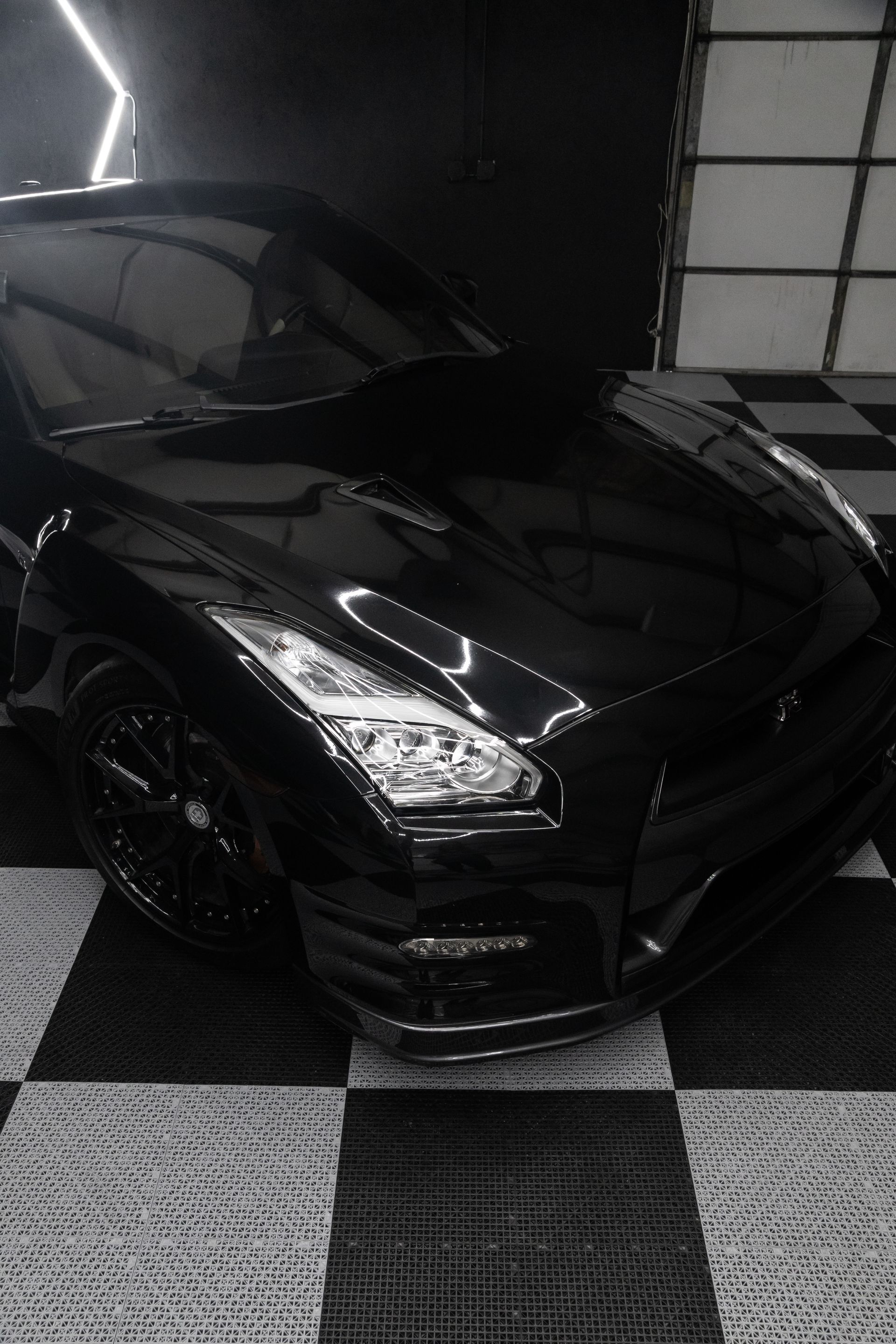 Black Nissan GT-R sports car parked on a checkered floor, with reflective highlights and a dark, glossy finish.