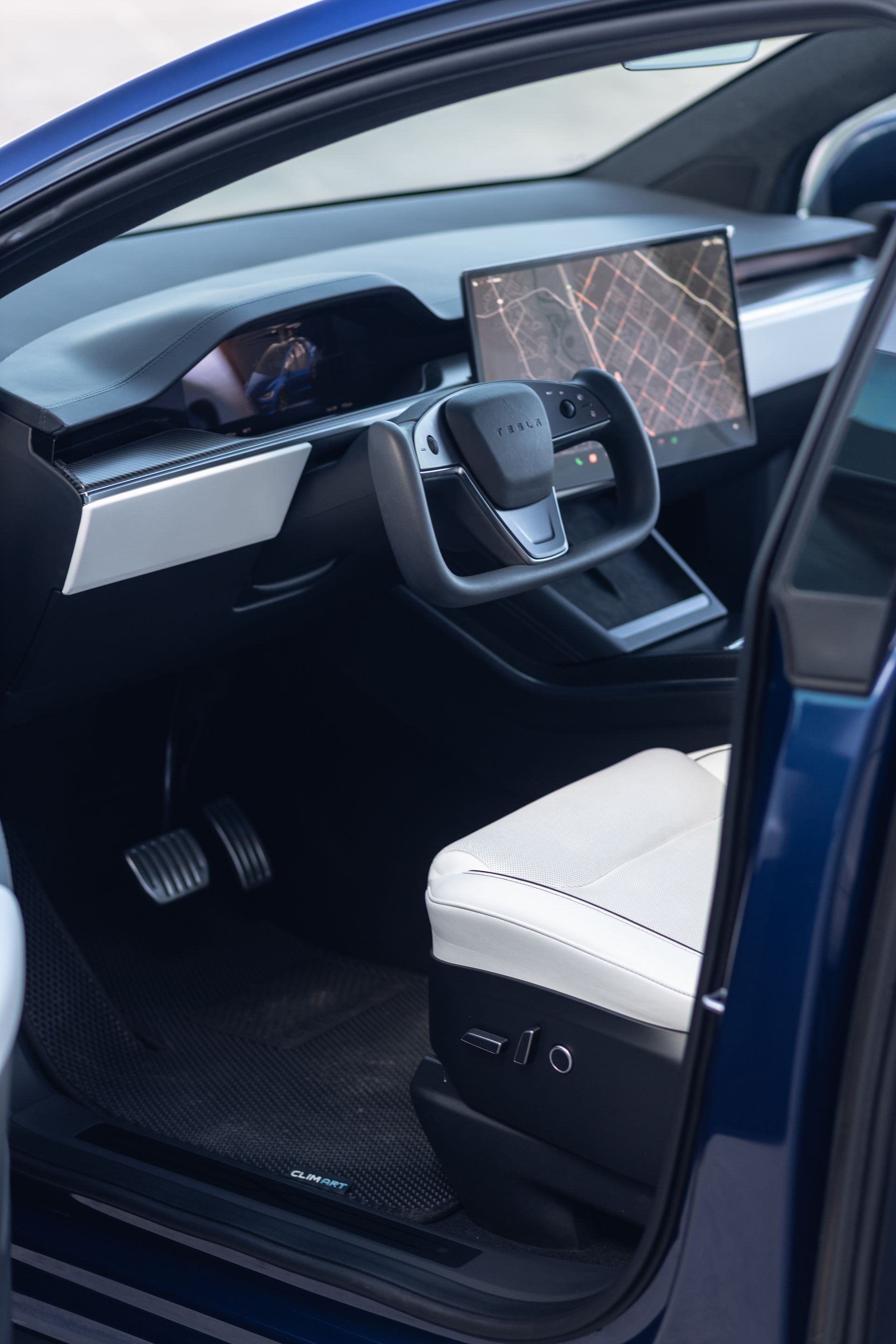 Blue car interior: white seat, black dashboard with large screen, steering wheel, open door.