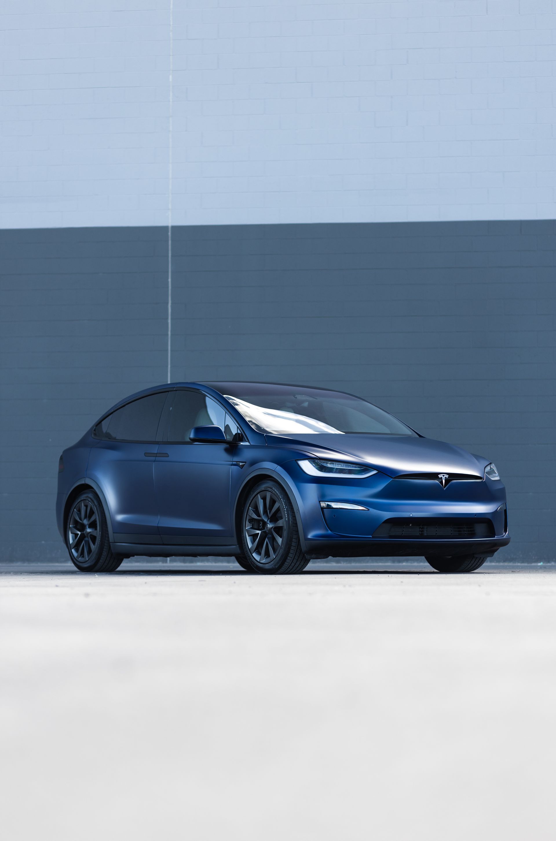 Blue Tesla Model X parked in front of a blue-gray building.