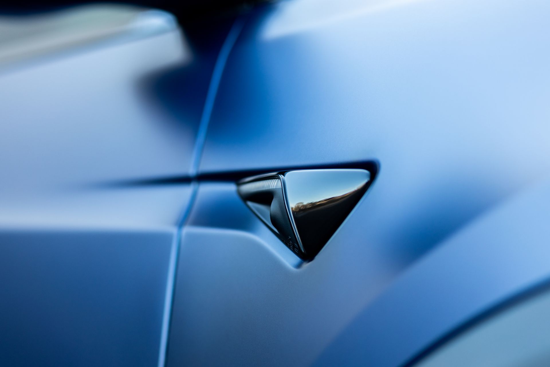 Close-up of a blue car's side, showing a shiny, black side camera.