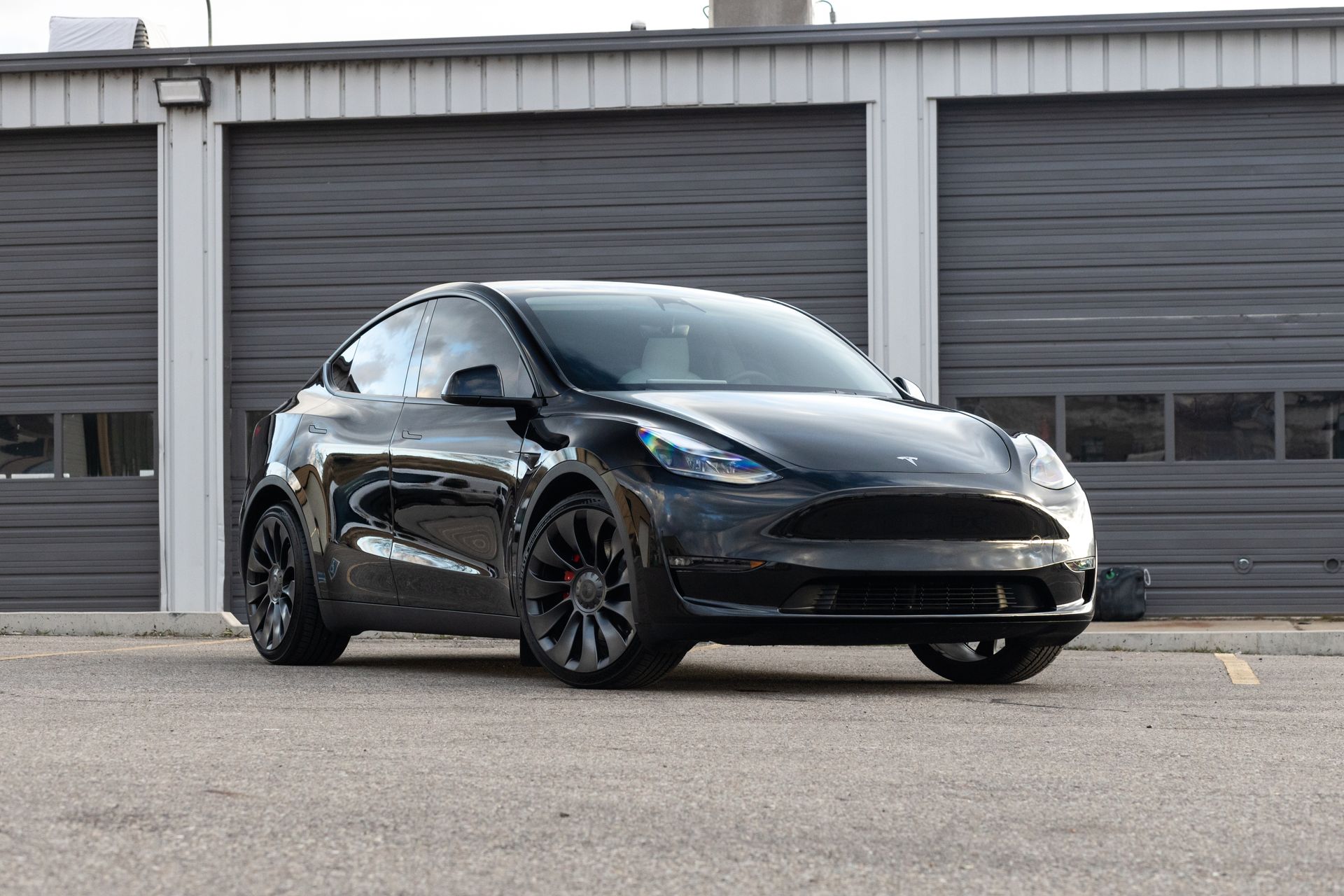 Black Tesla Model Y parked in front of three gray garage doors.