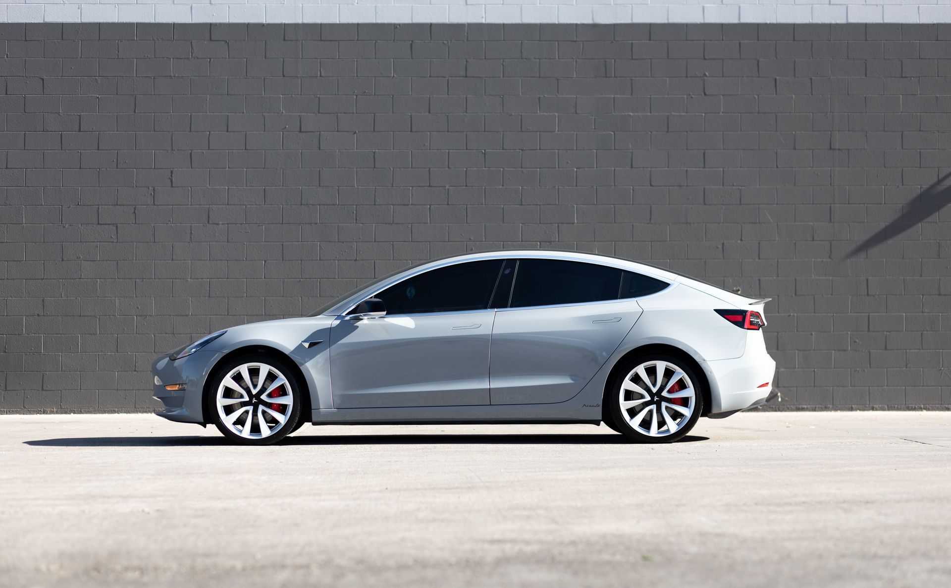 Gray Tesla Model 3 parked against a gray brick wall.