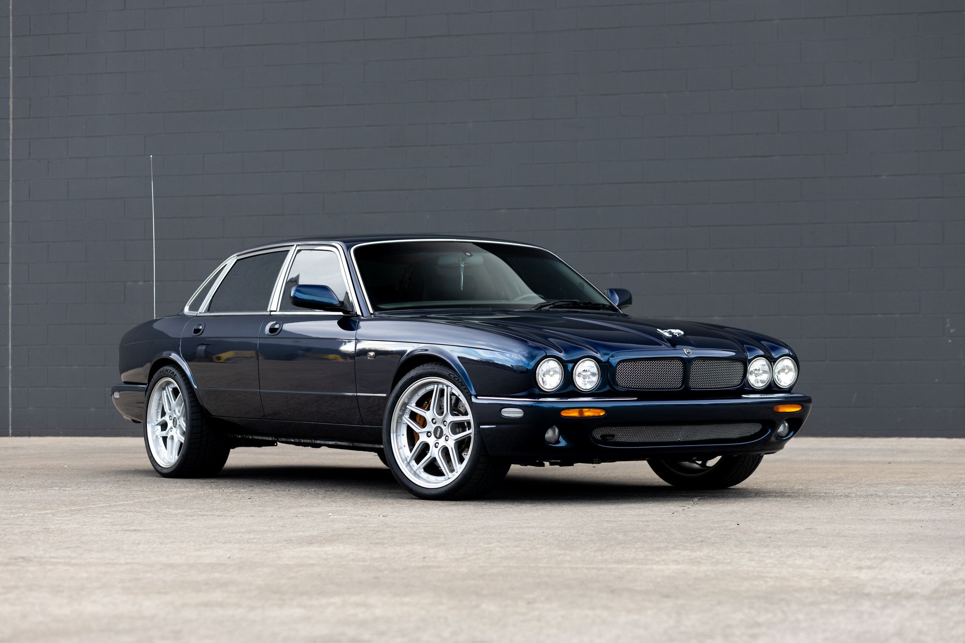 Dark blue Jaguar sedan on a gray surface with a dark wall background.