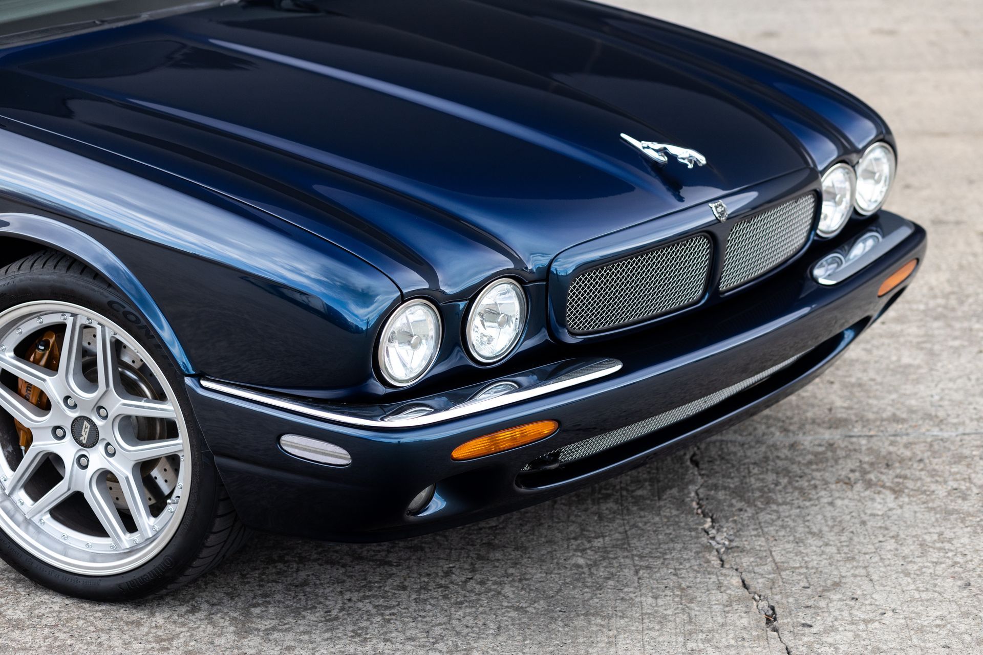 Blue Jaguar car with silver wheels. Front view showing headlights, grill, and hood with logo.