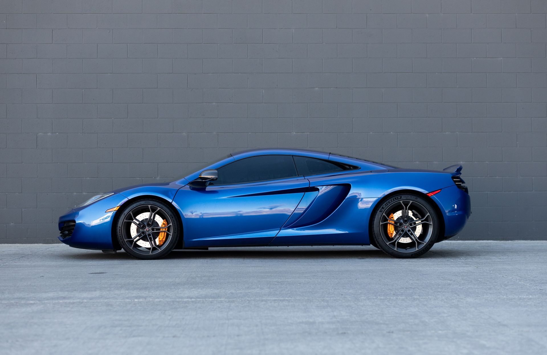 Blue McLaren sports car parked in front of a gray wall.