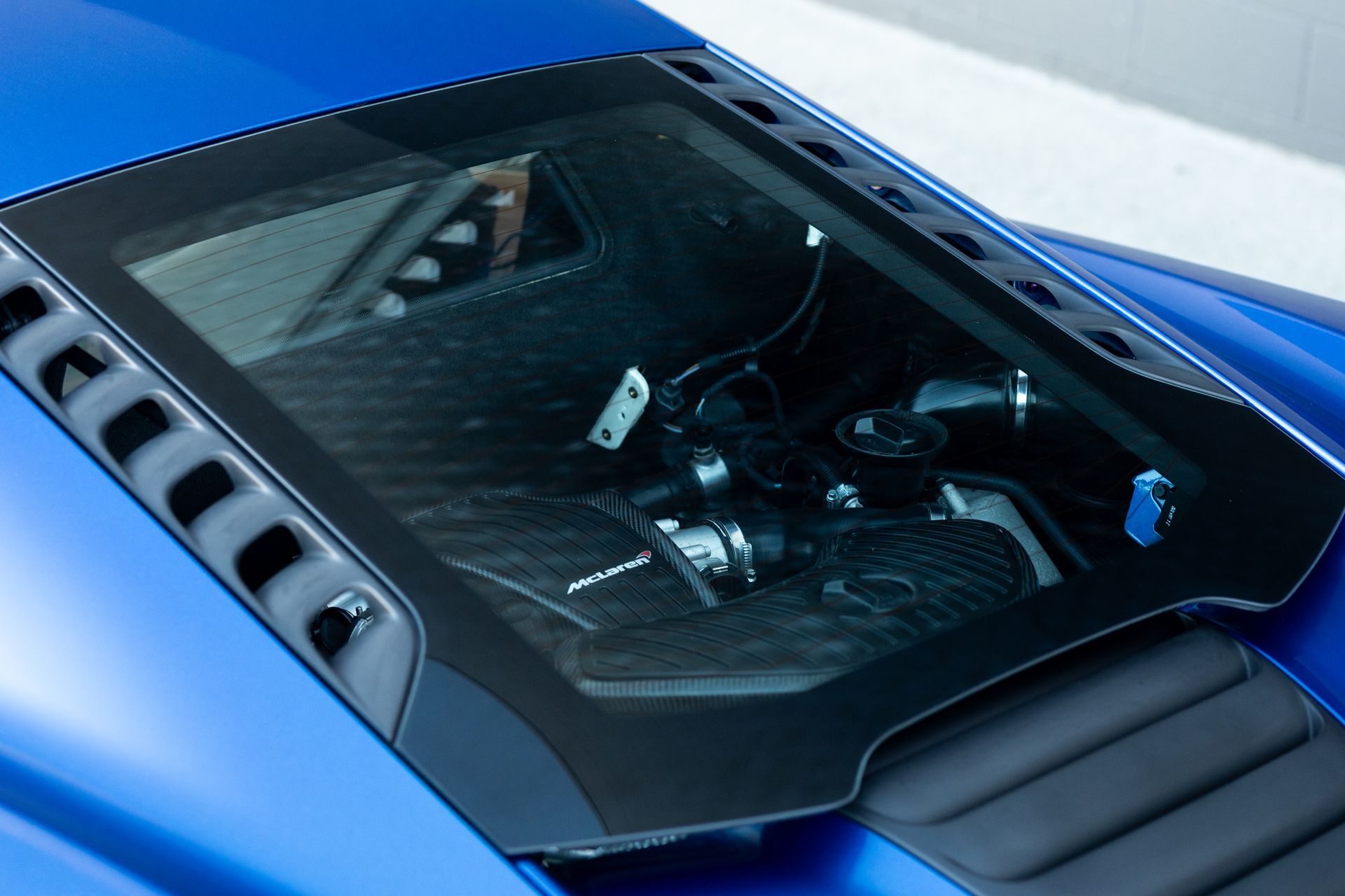 Blue sports car rear with engine visible through glass panel.