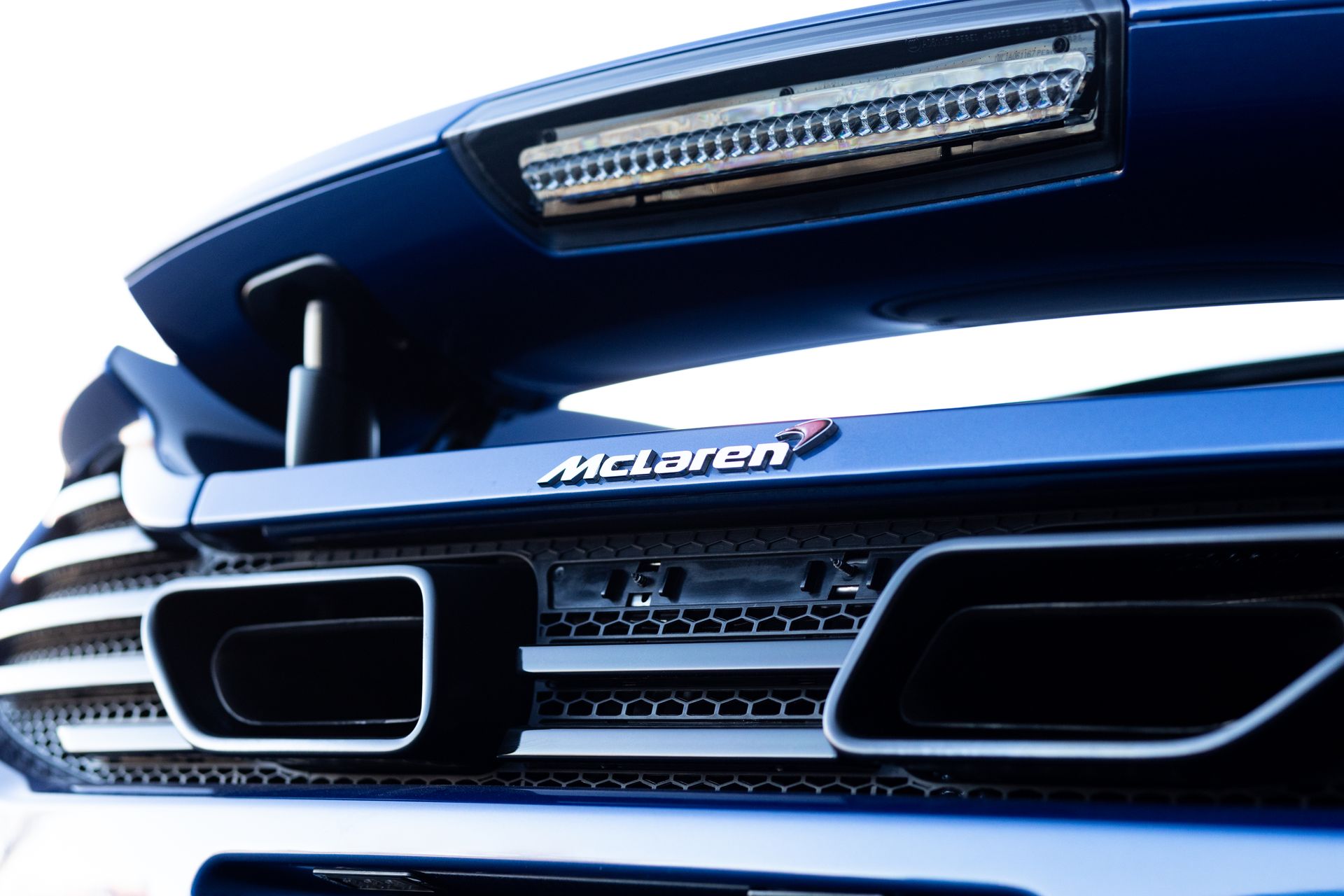 Rear view of a blue McLaren sports car, featuring the exhaust, spoiler, and the McLaren logo.