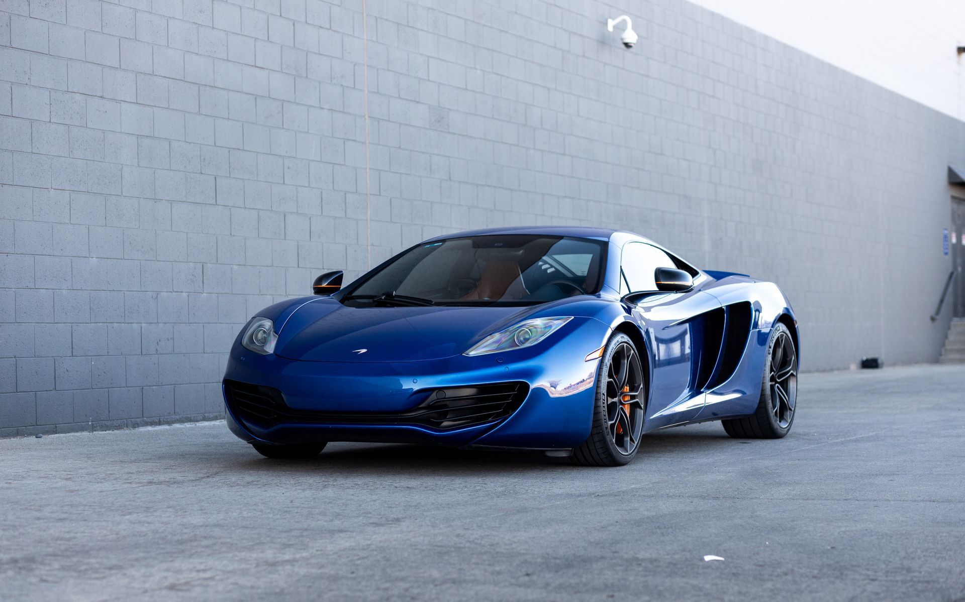 Blue McLaren sports car parked in front of a gray brick wall.