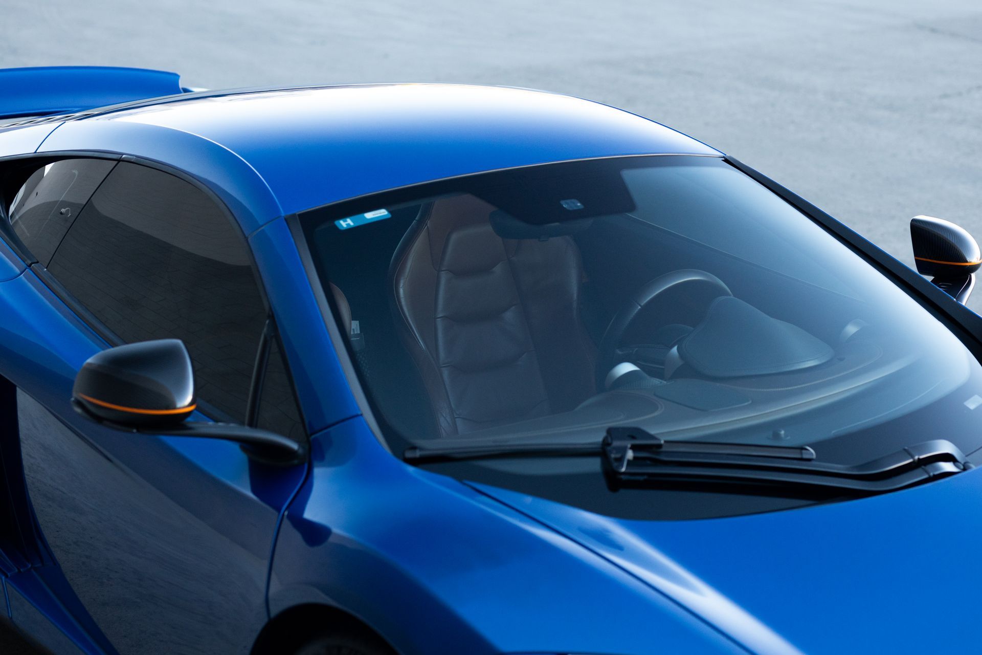 Blue McLaren sports car, partial view, side profile. Shows windshield, door, mirror, and interior.