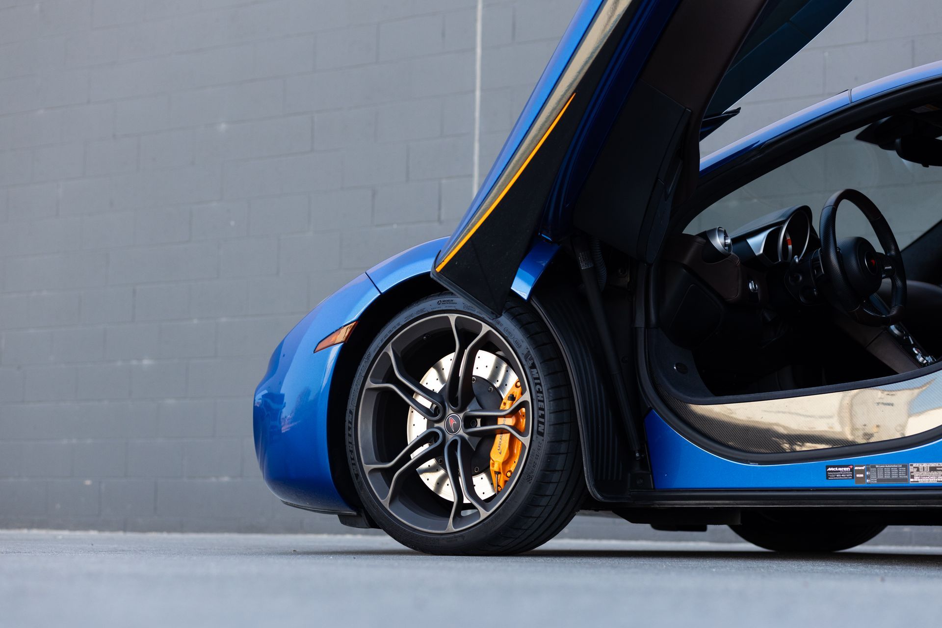 Blue sports car with gullwing door open, revealing interior details and a large wheel.