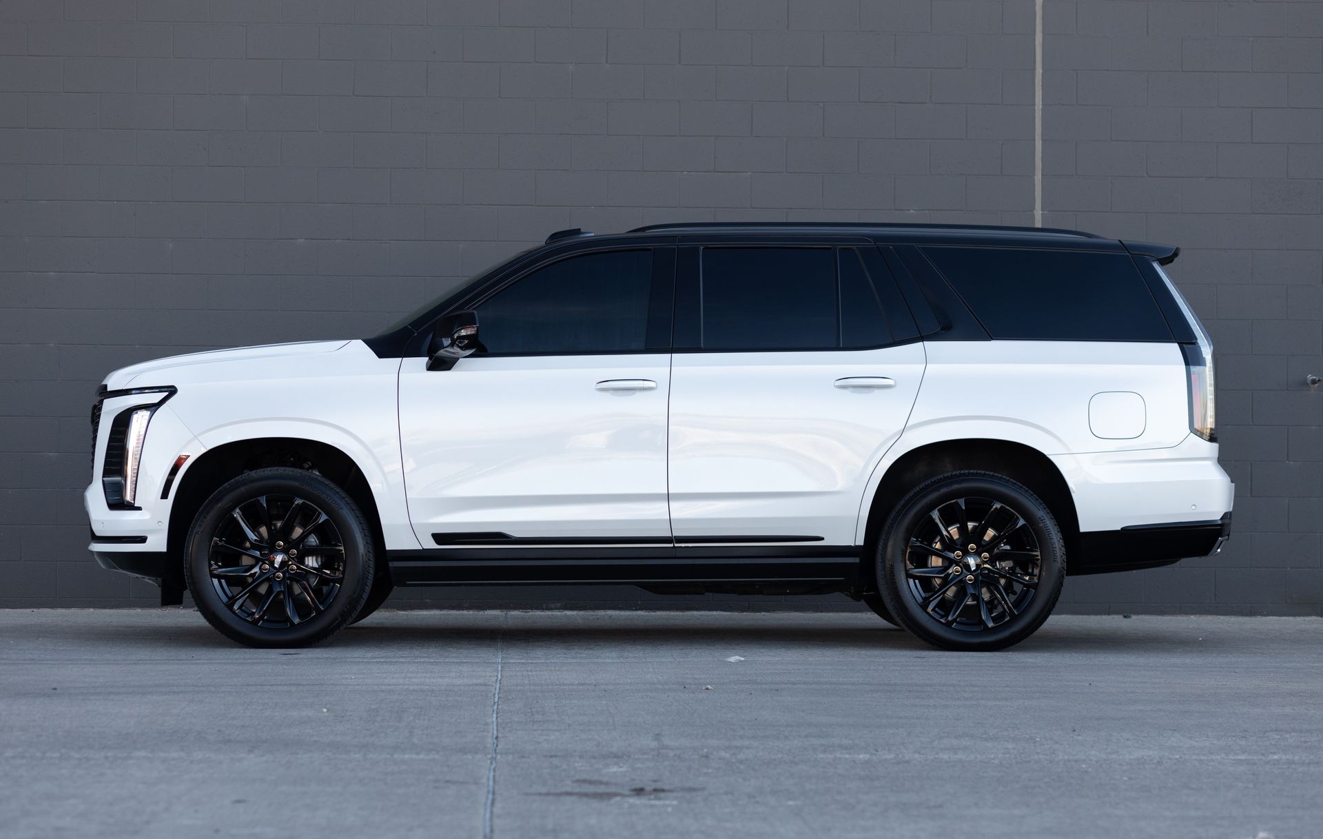 White Cadillac Escalade SUV with black wheels and roof against a grey wall.