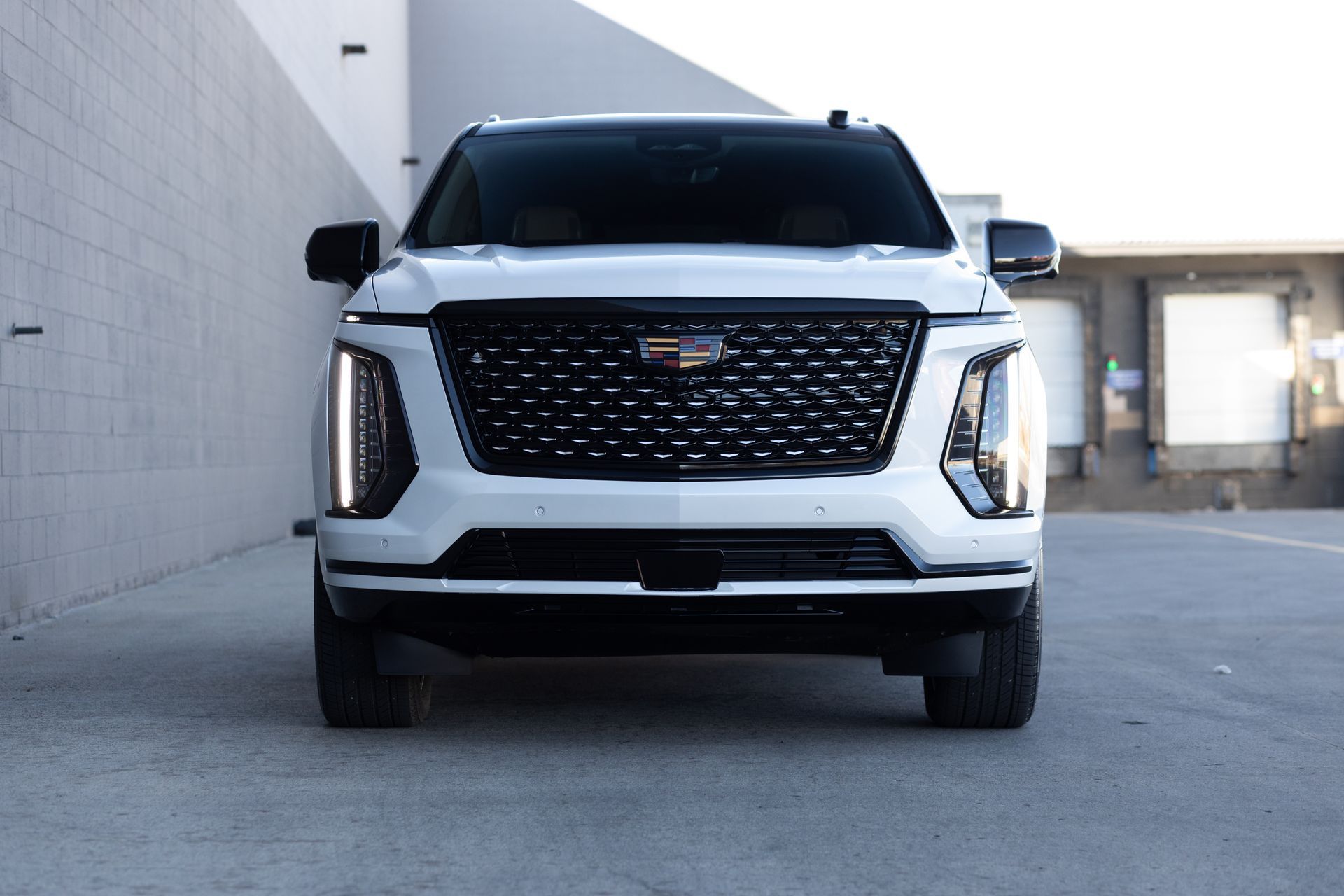 White Cadillac SUV, front view, black grille and trim, parked near a building.