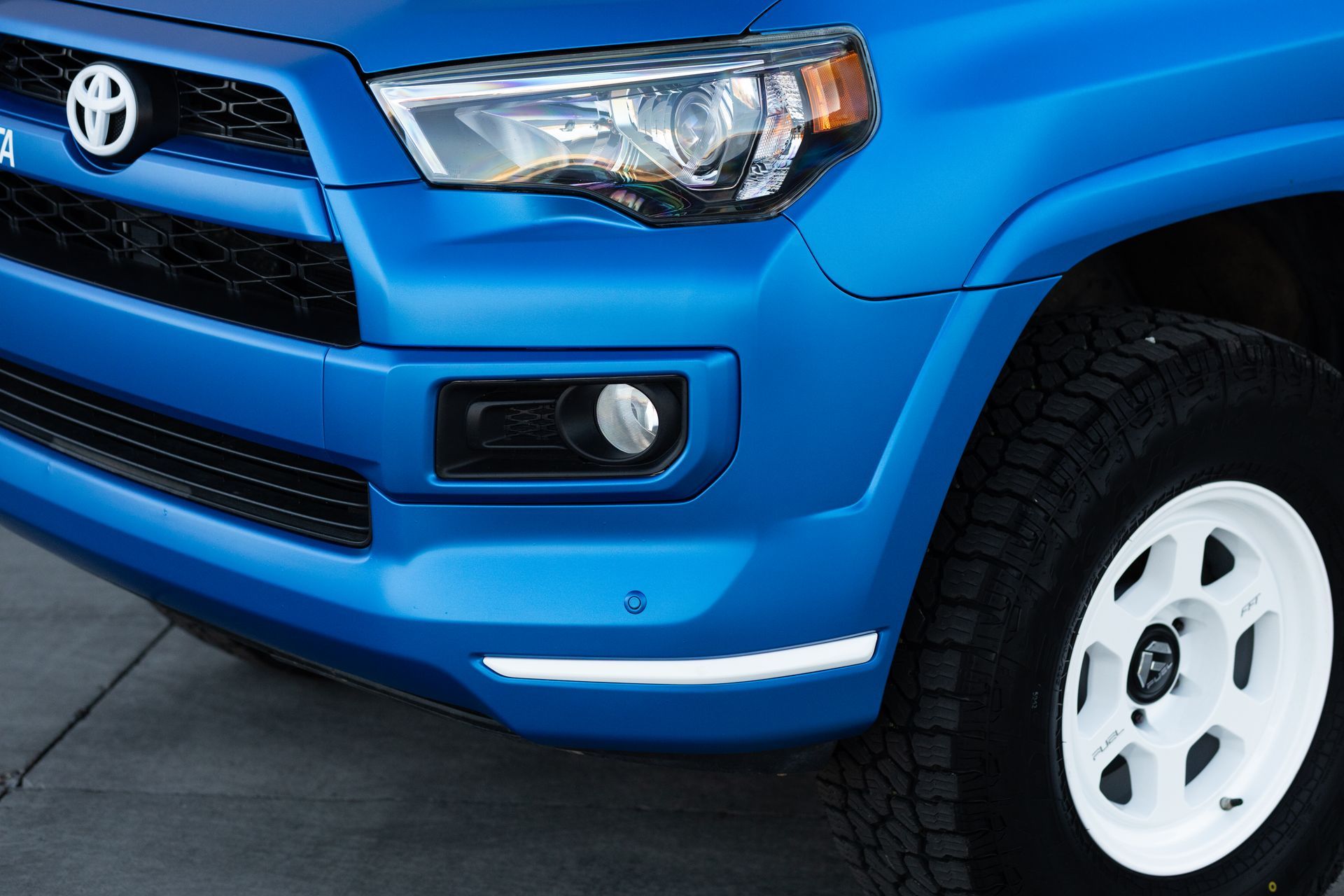Blue Toyota 4Runner front end with a white rimmed tire and white fog light.