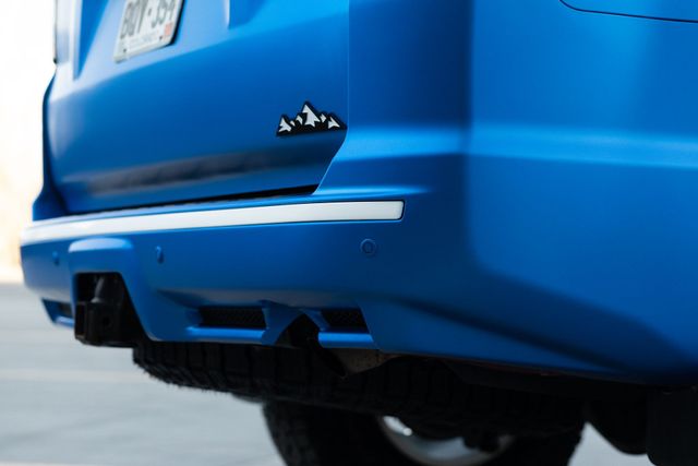 Blue car's rear bumper with a mountain peak logo, chrome trim, and black exhaust detail.