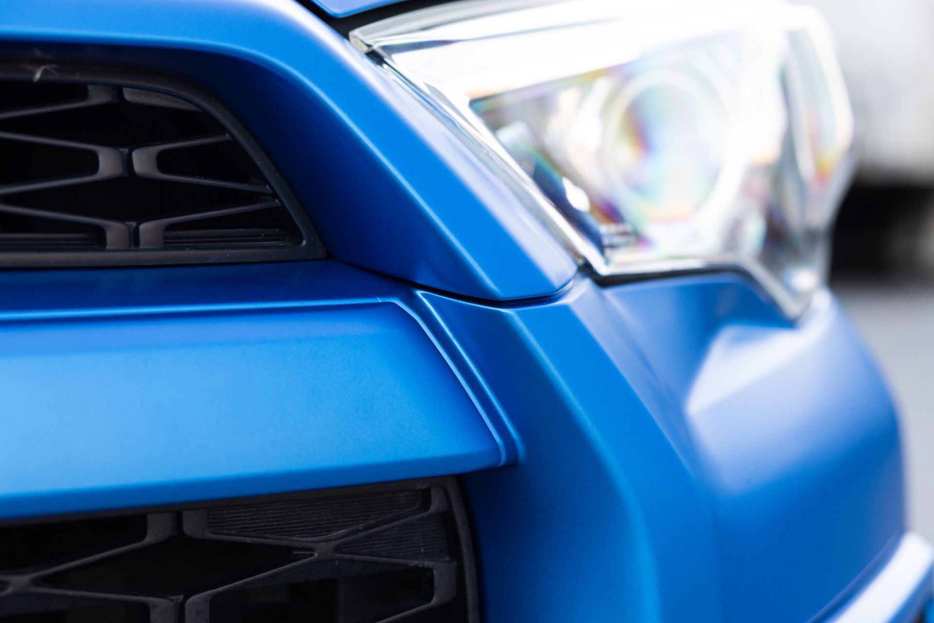 Blue car's front with a black grille and a headlight.