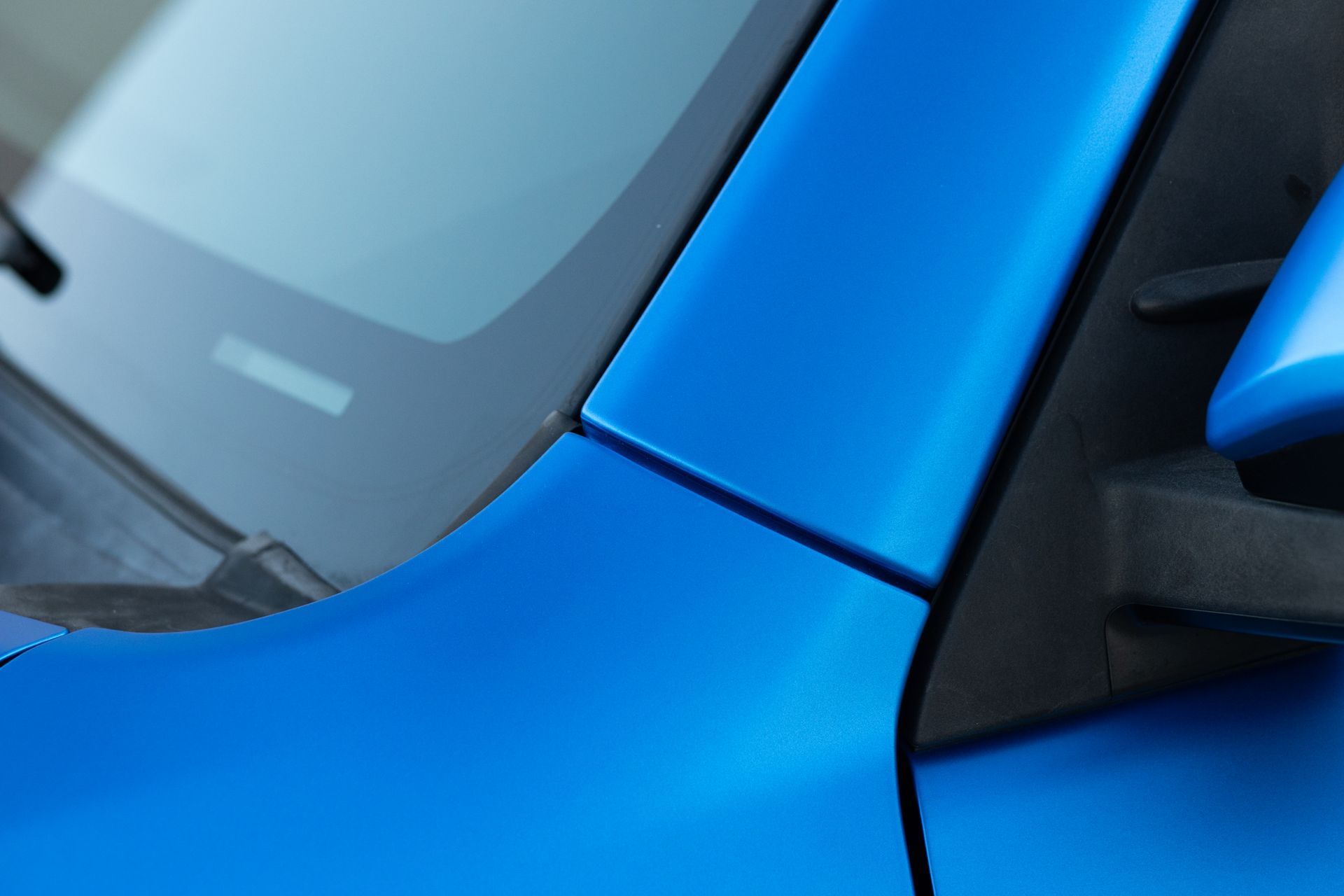 Blue car's body, detail shot: front panel, windshield, and side mirror.