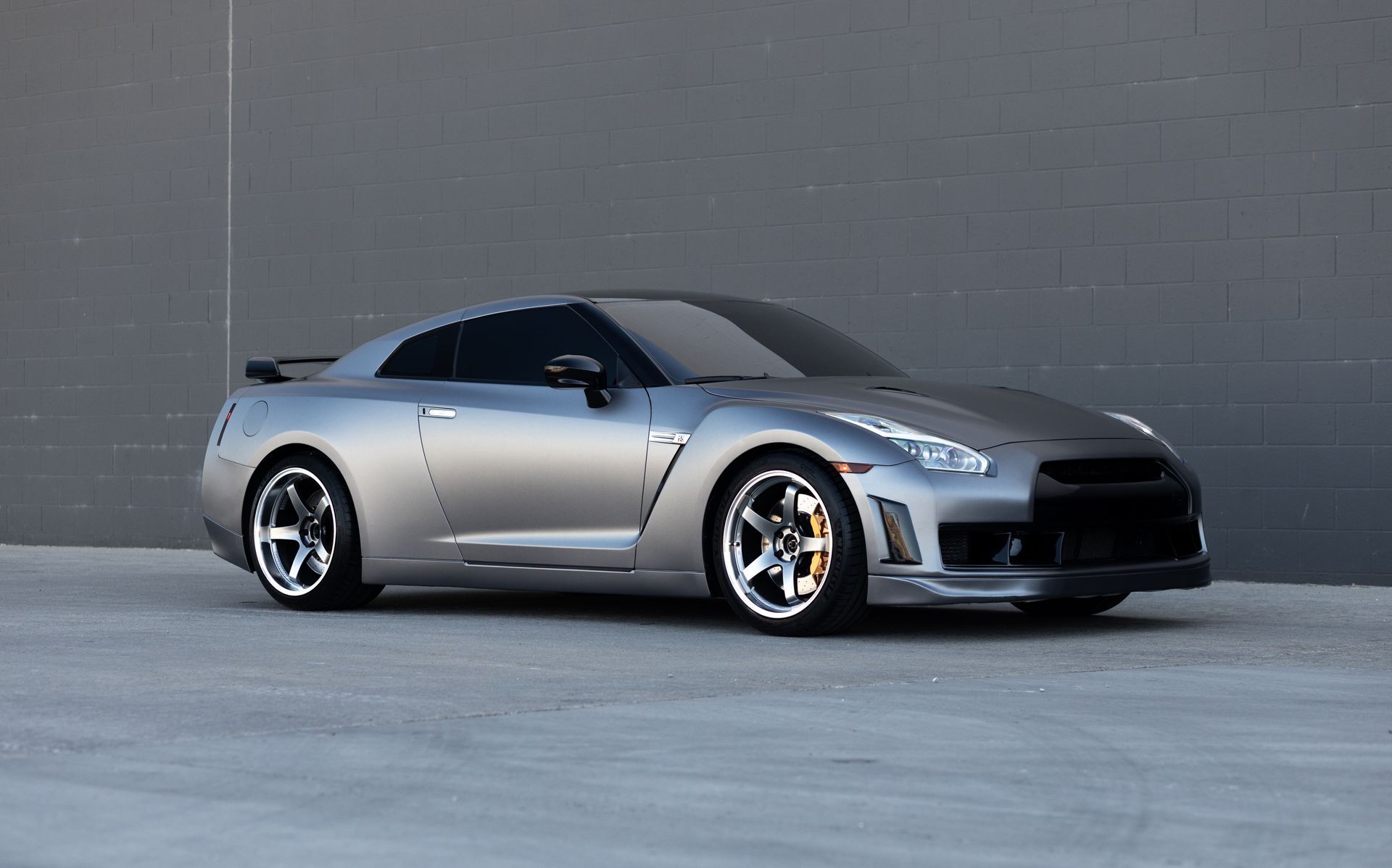 Silver Nissan GT-R sports car parked in front of a gray wall.