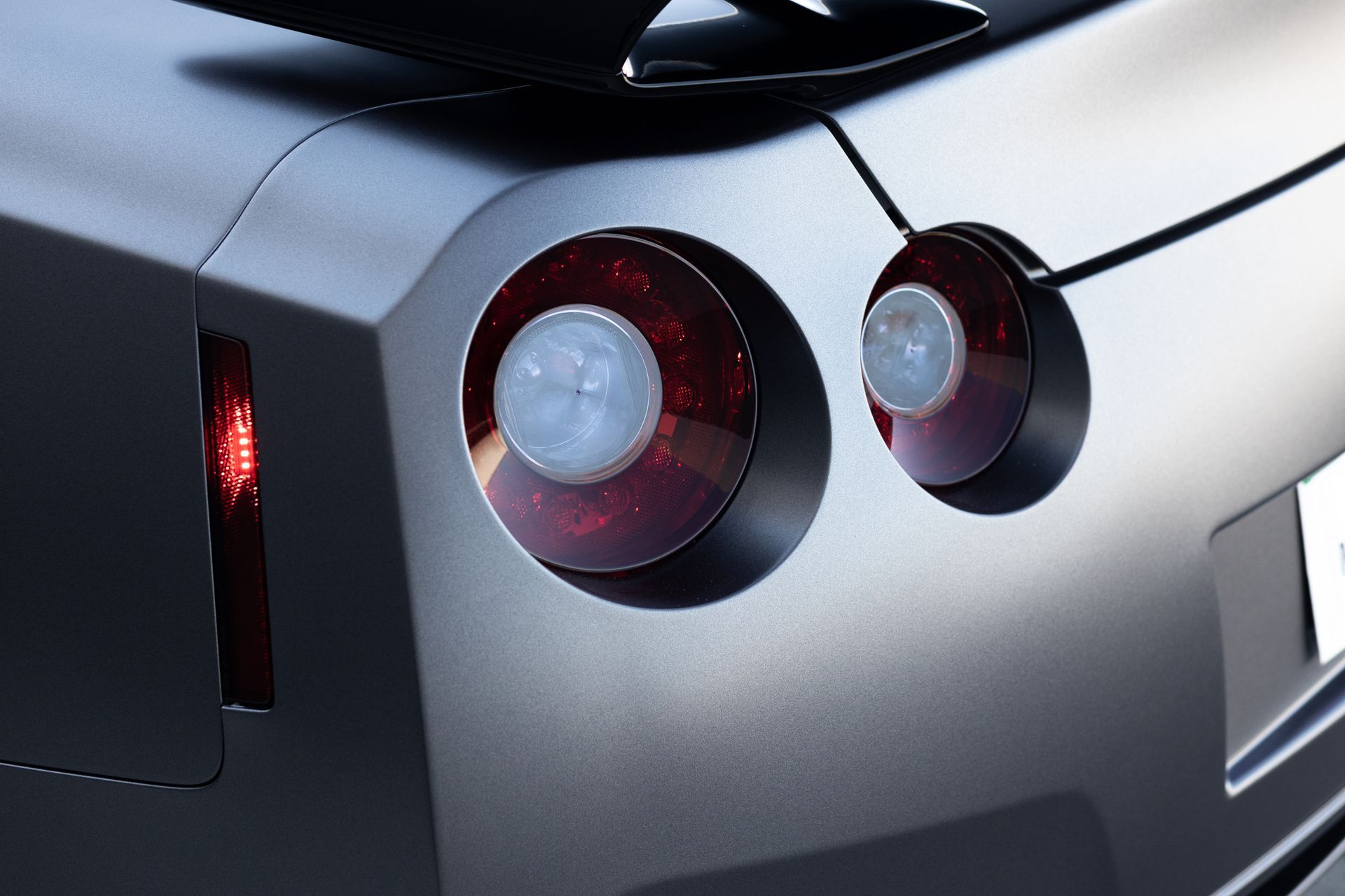 Rear of a gray sports car with circular red taillights and a thin vertical brake light.