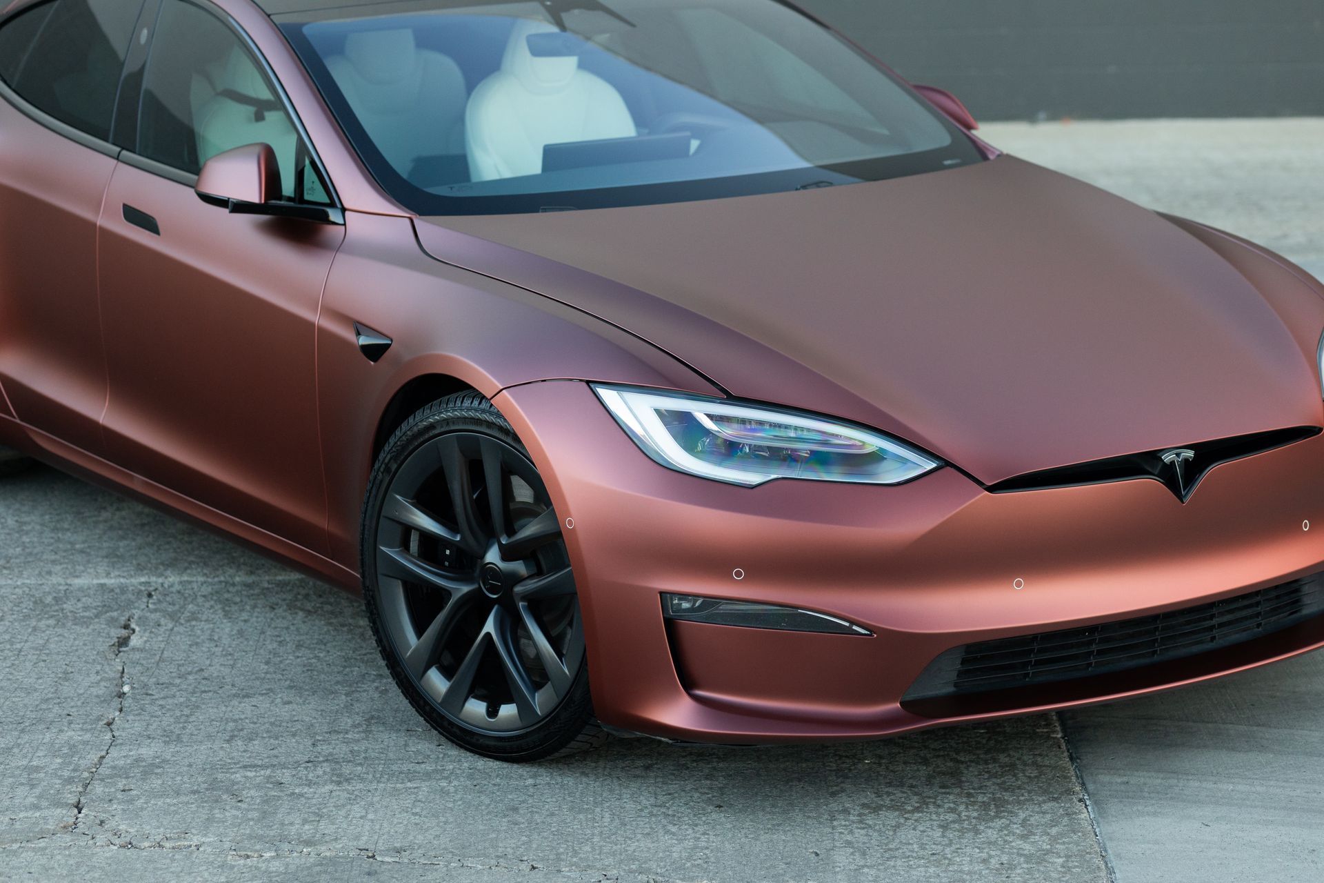 Brown Tesla Model S electric car parked on a concrete surface.