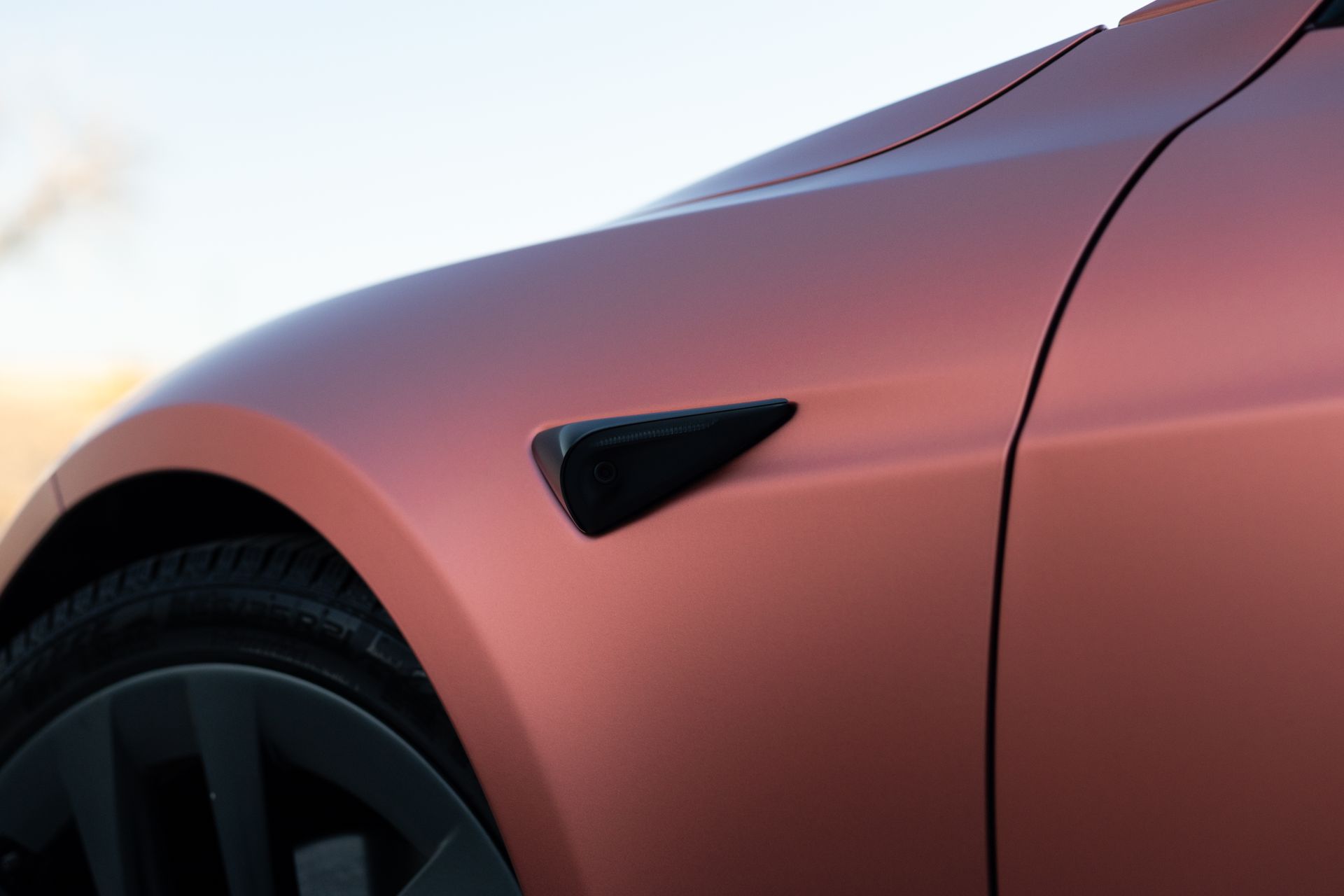Close-up of a salmon-colored Tesla Model S front fender with a black side marker light and black wheel.